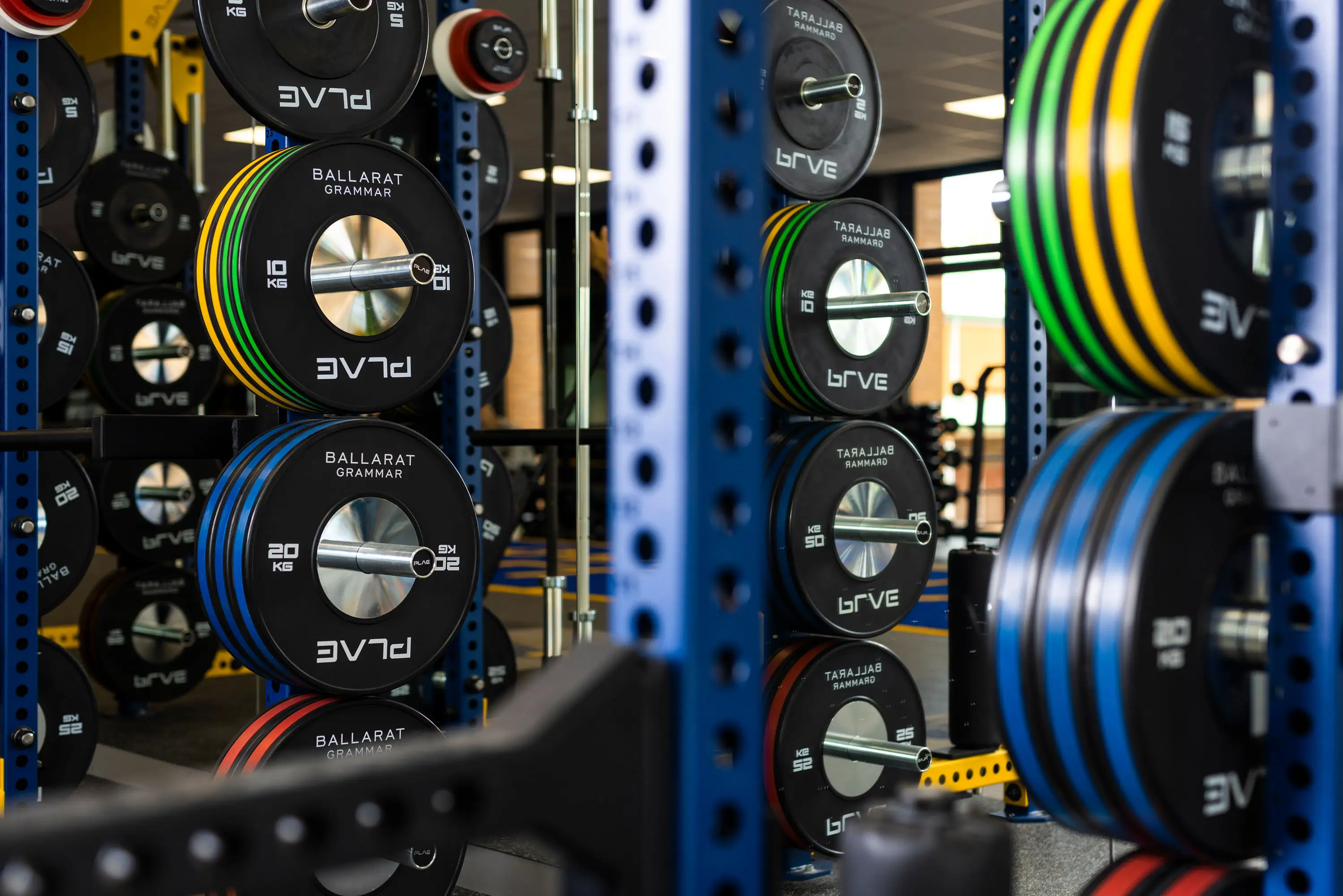 Colour-coded PLAE competition bumper plates branded for Ballarat Grammar, racked on blue PLAE ICON X uprights