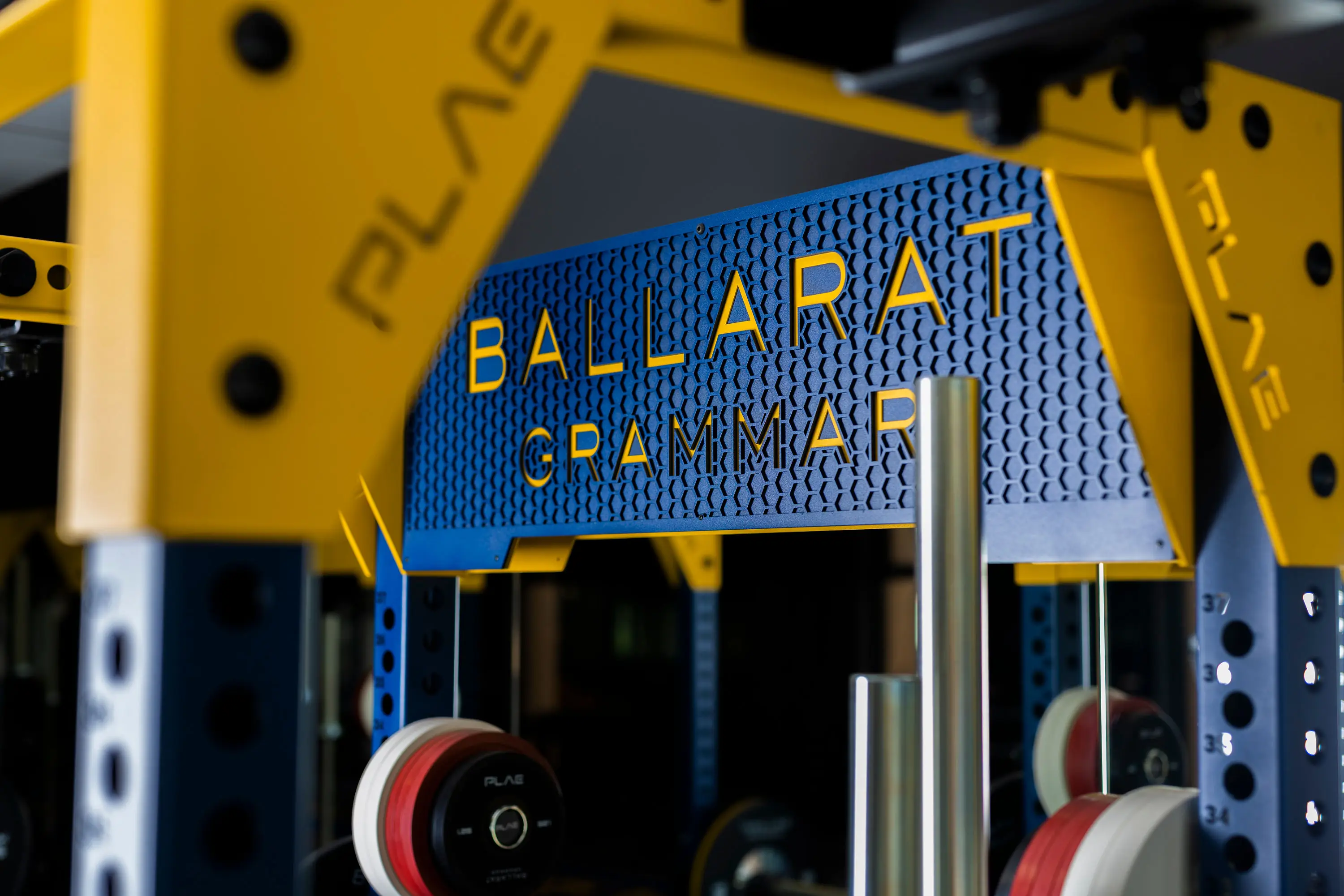 Yellow-and-blue PLAE ICON X rack canopy laser-cut with the Ballarat Grammar name in the school's PLAE performance gym