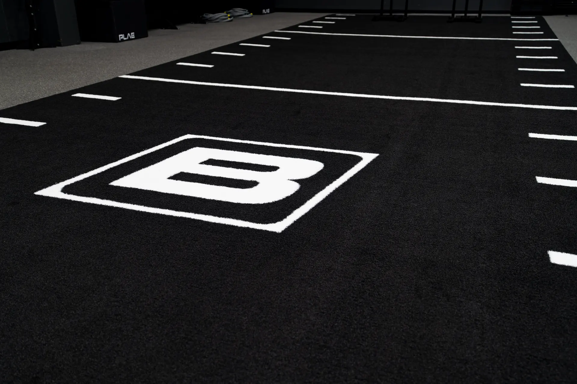 Black PLAE ATTACK turf sprint track with yard markers and the Bare Performance Nutrition B logo at BPN headquarters