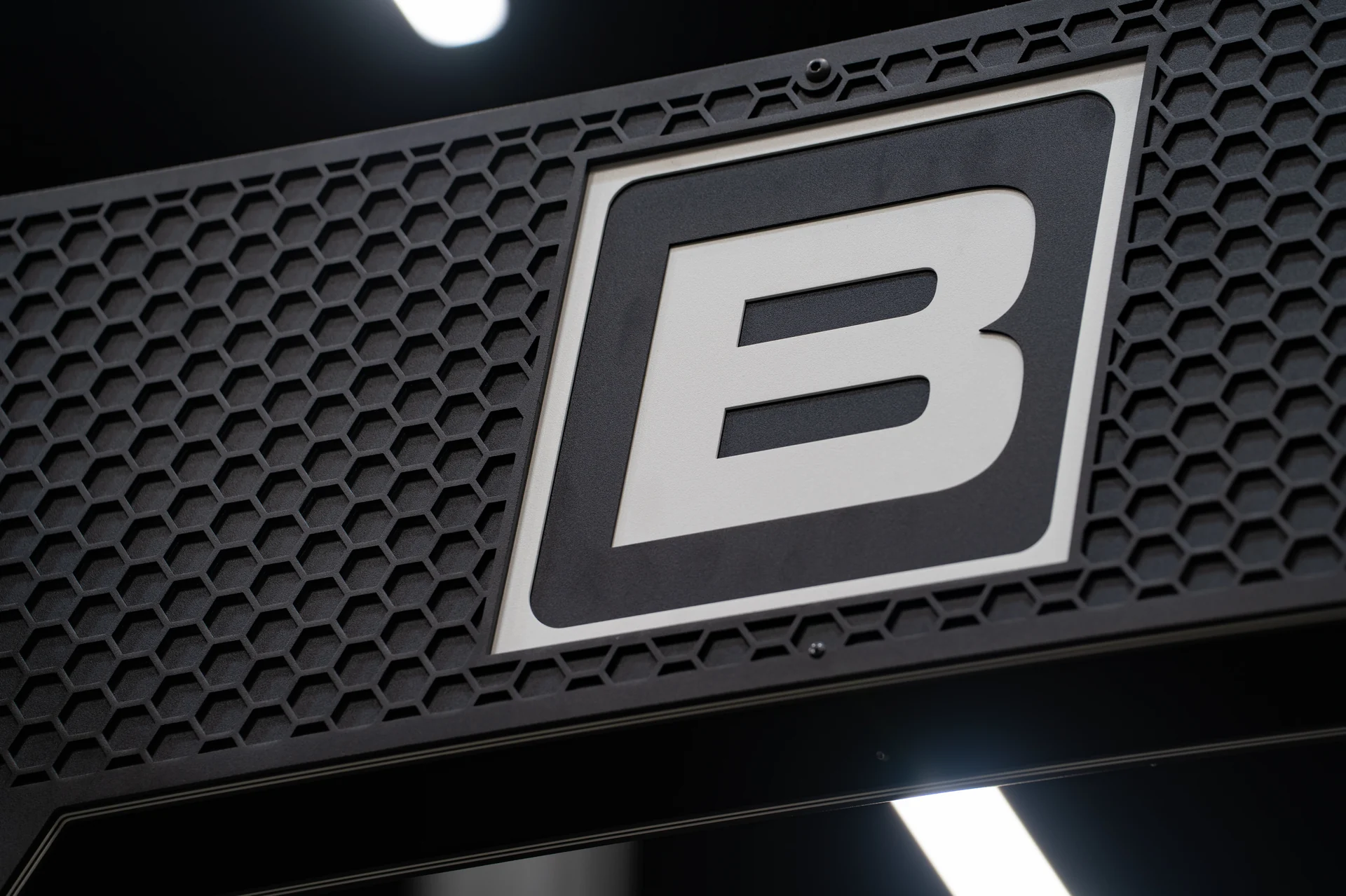 Close-up of the Bare Performance Nutrition B badge set into a hex-mesh PLAE ICON X rack crown