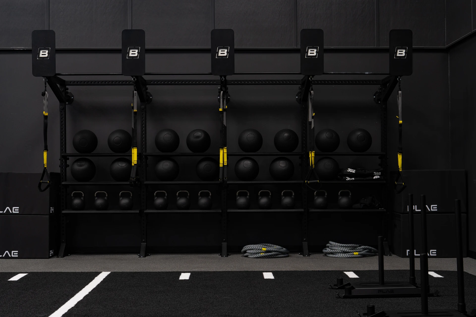 Blackout PLAE functional wall rack of slam balls, kettlebells and TRX with battle ropes and a sled on the ATTACK turf lane