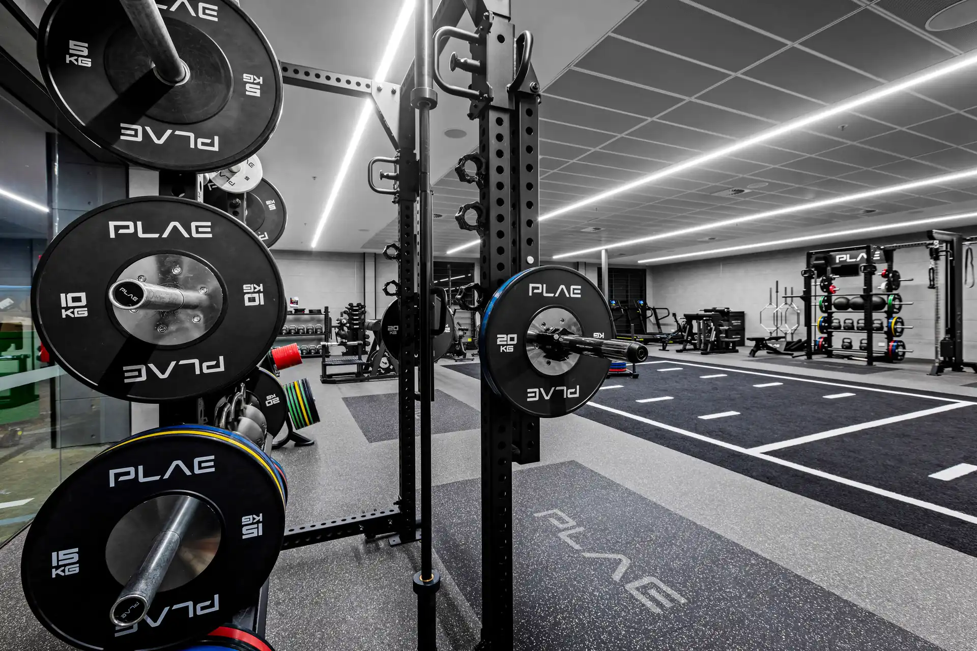 PLAE ICON X rack and bumper plate tree with slam ball and kettlebell storage beneath a PLAE screen at Fitness First Richmond