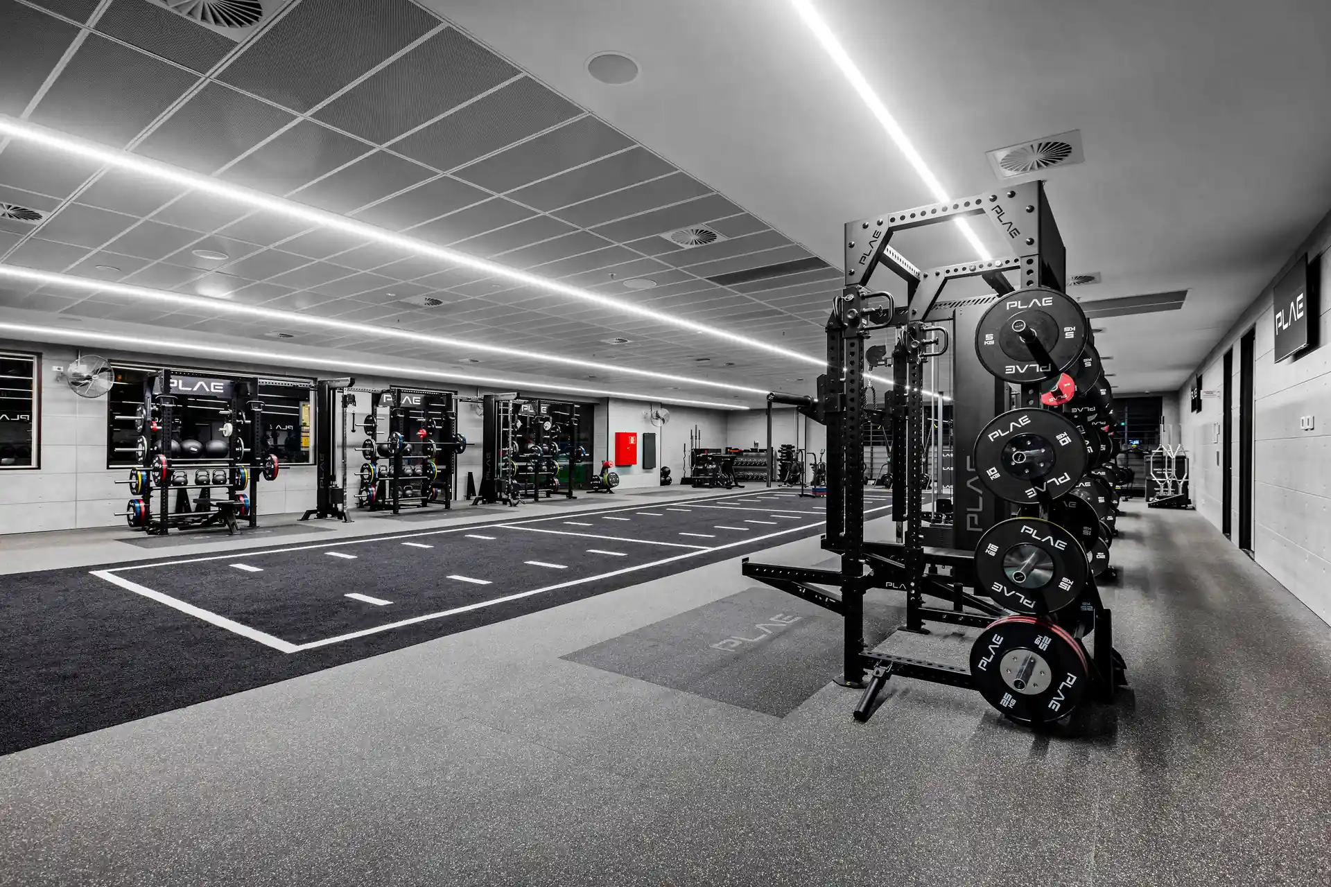 Fitness First Richmond gym with PLAE ICON X racks lining the walls and a marked ATTACK turf sprint track running through the centre