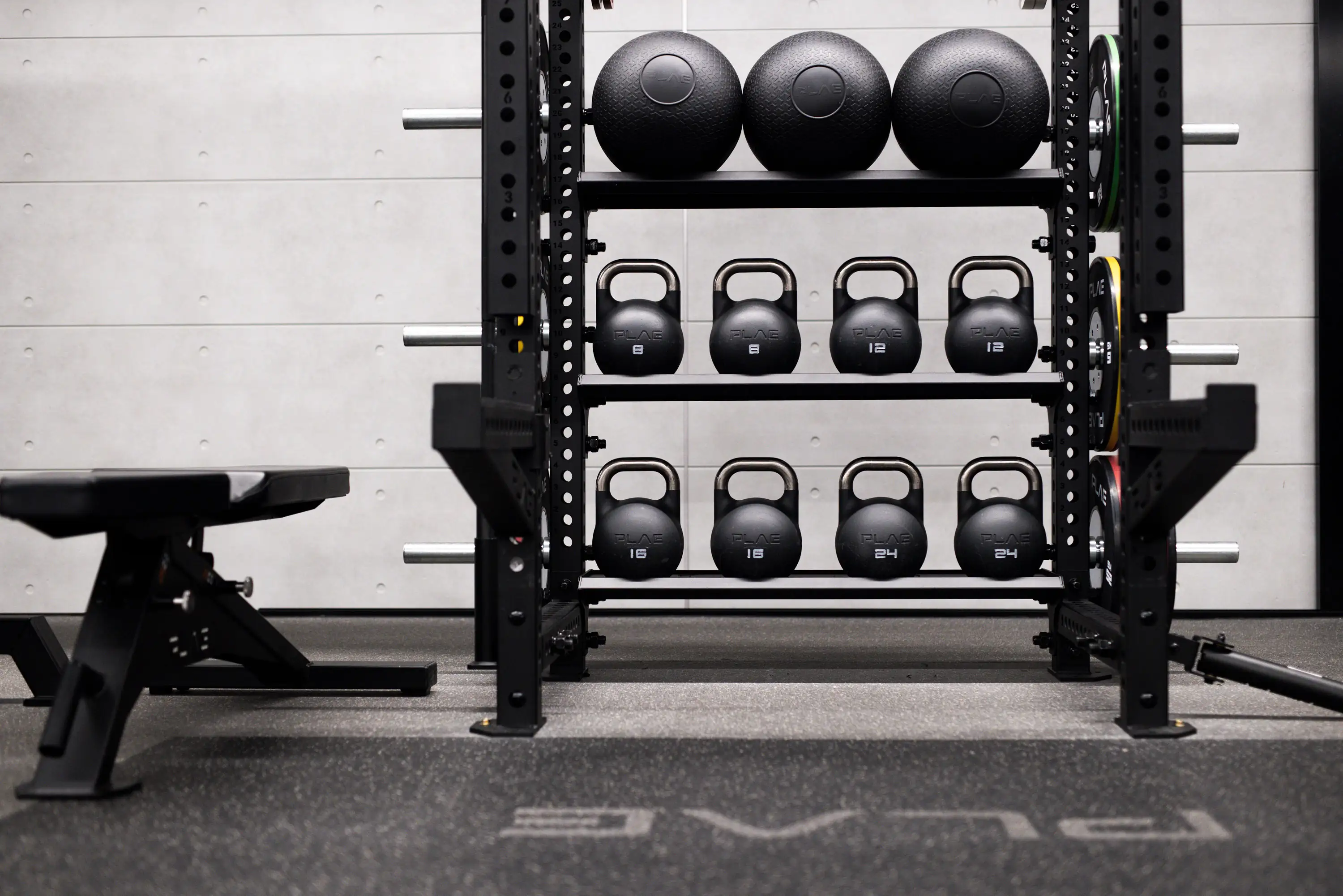 Front view of a PLAE storage rack with slam balls and calibrated kettlebells, PLAE bumper plates on the uprights