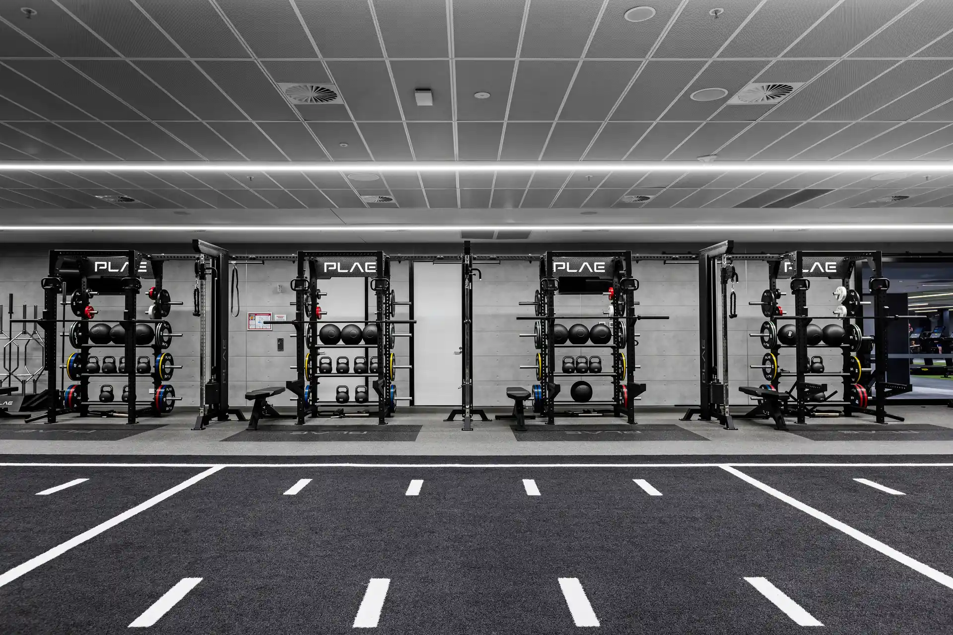 Row of PLAE ICON X racks stocked with slam balls, kettlebells and calibrated bumper plates beside the ATTACK turf track at Fitness First Richmond