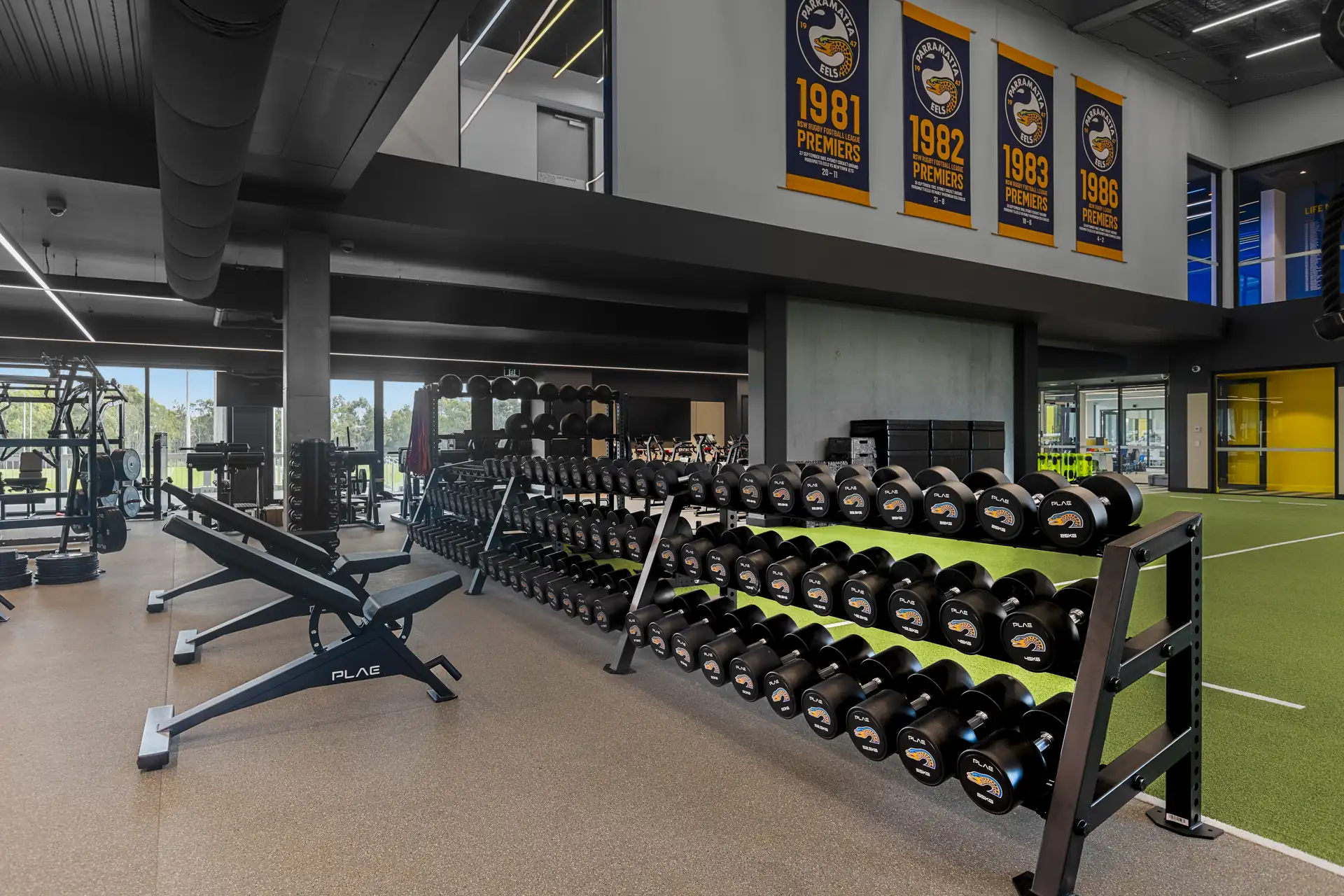 Rack of Parramatta Eels branded PLAE dumbbells and a bench beneath the club's premiership banners at the Eels Centre of Excellence