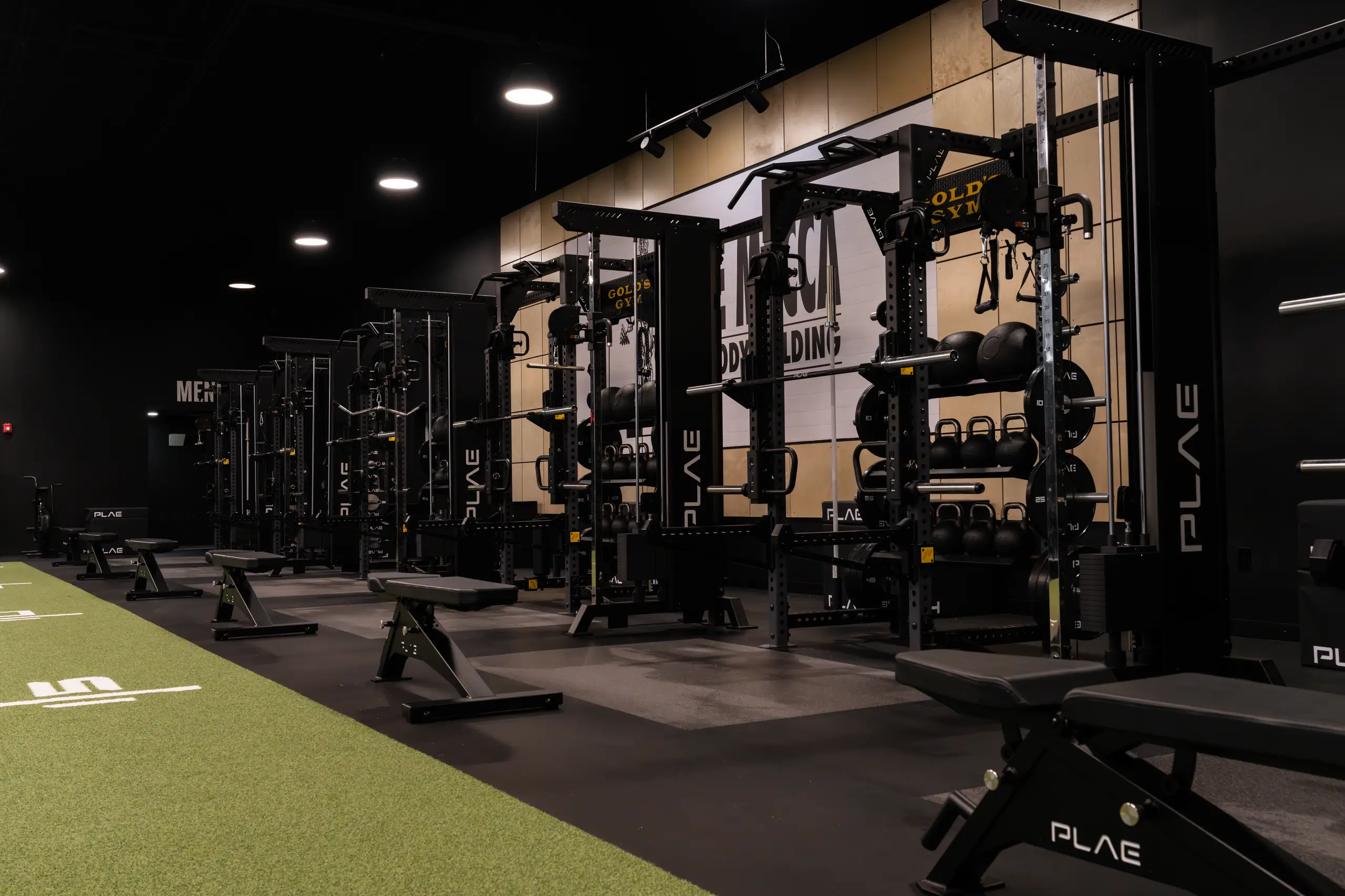 PLAE ICON X racks with Gold's Gym crowns loaded with bumper plates and kettlebells along the Mecca of Bodybuilding wall in Austin
