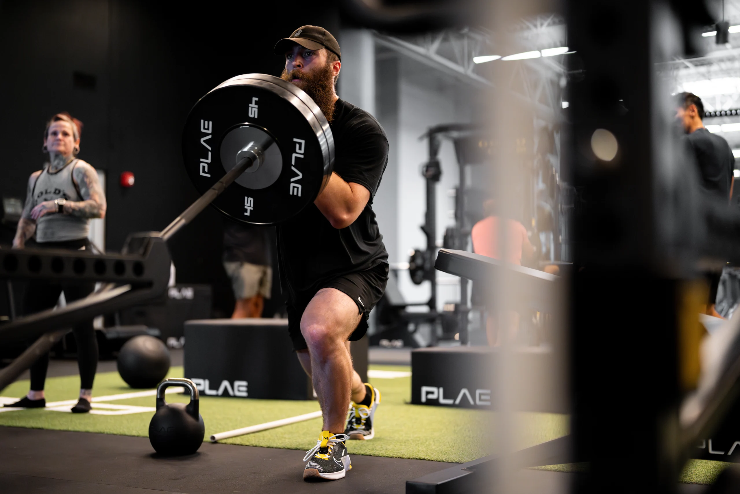 Athlete performing a barbell lunge with PLAE plates on the green ATTACK turf during training at Gold's Gym Austin