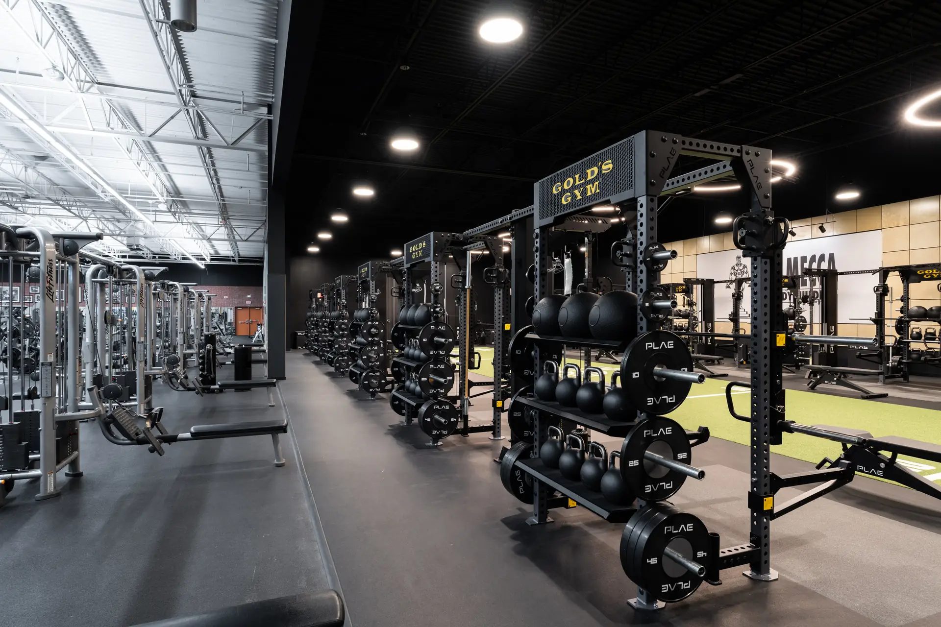 Row of Gold's Gym PLAE ICON X racks with PLAE plates and kettlebells beside the turf track and cable machines in Austin