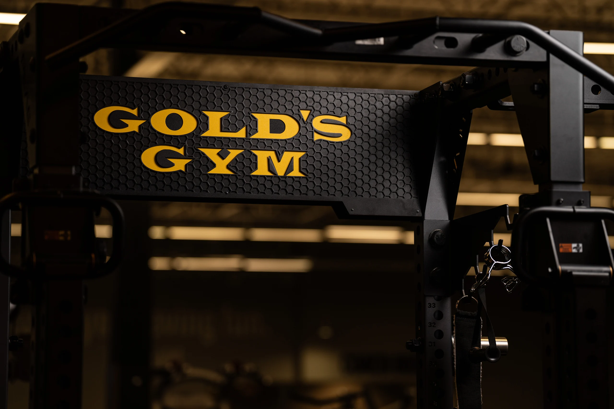 Gold's Gym name in gold on a black PLAE ICON X rack canopy, a signature branded feature at Gold's Gym Austin
