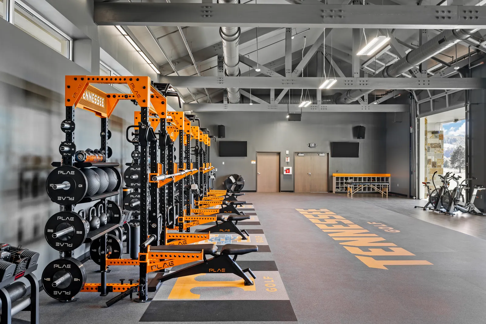 PLAE-equipped Tennessee golf weight room with custom racks, logo flooring and a roll-up glass door opening to mountain views.