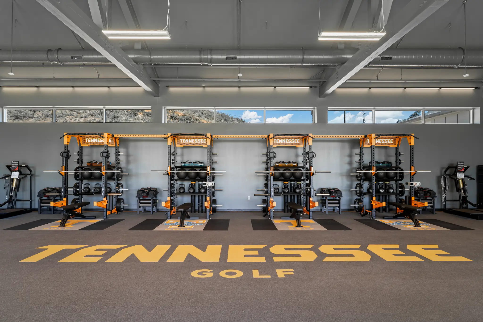 Four matching PLAE Tennessee squat racks along the wall of the Vols golf weight room above a large "Tennessee Golf" PLAE floor inlay.