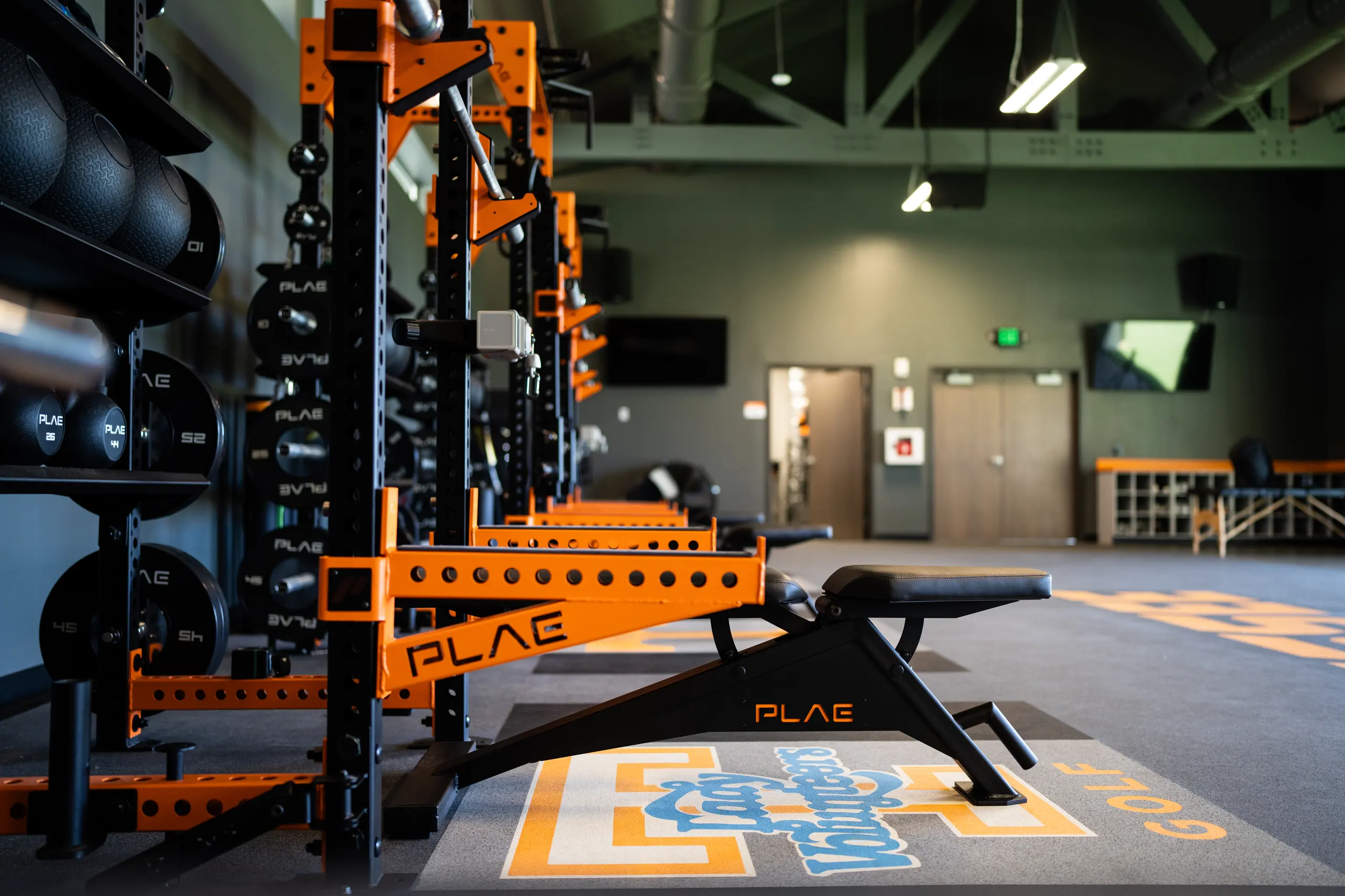 PLAE ICONx racks, adjustable benches and medicine ball storage lining the Lady Volunteers golf weight room with custom PLAE logo flooring.