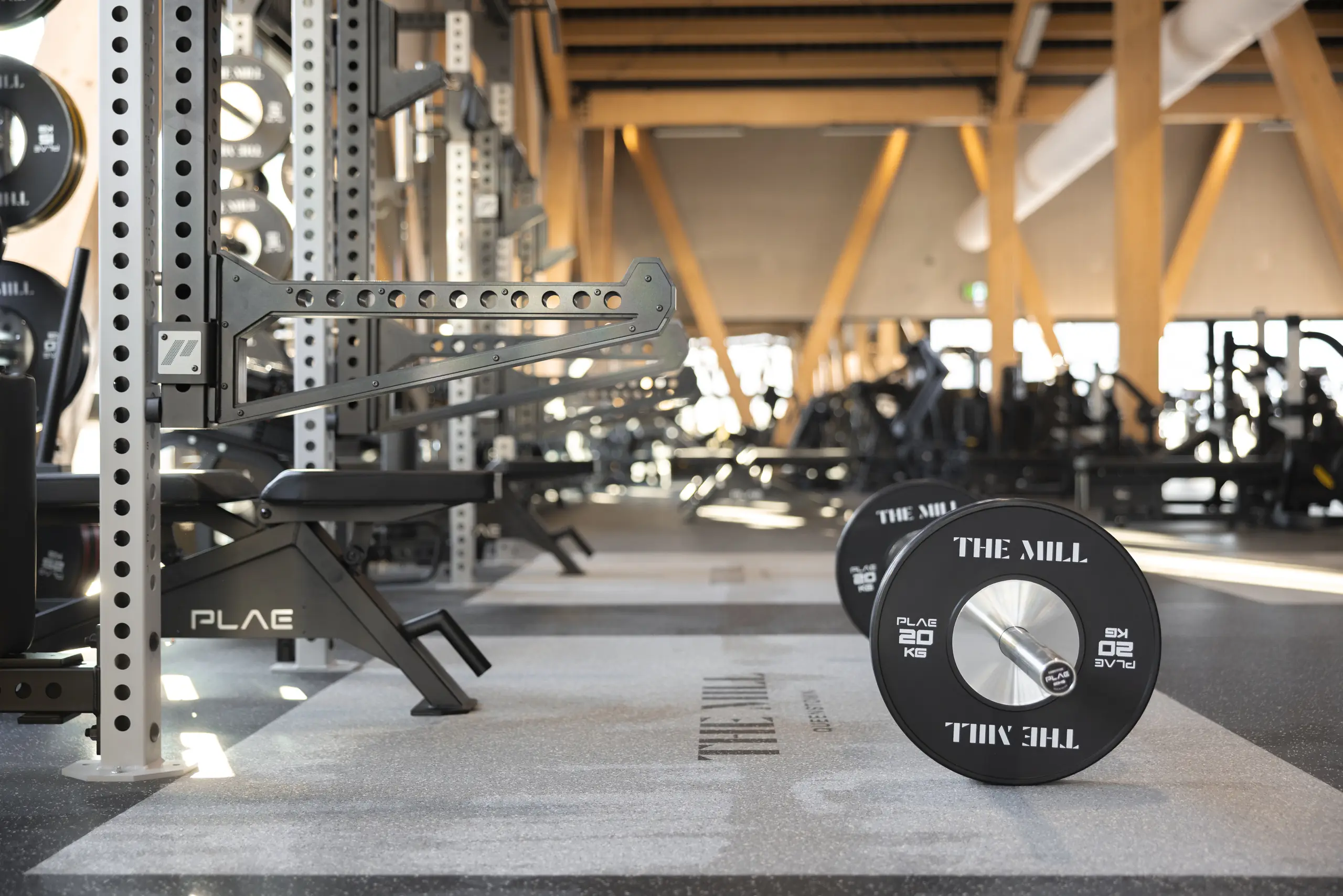 PLAE ICONx rack upright and spotter arm beside a custom "The Mill" 20kg PLAE bumper plate loaded on a barbell at The Mill, Queenstown.