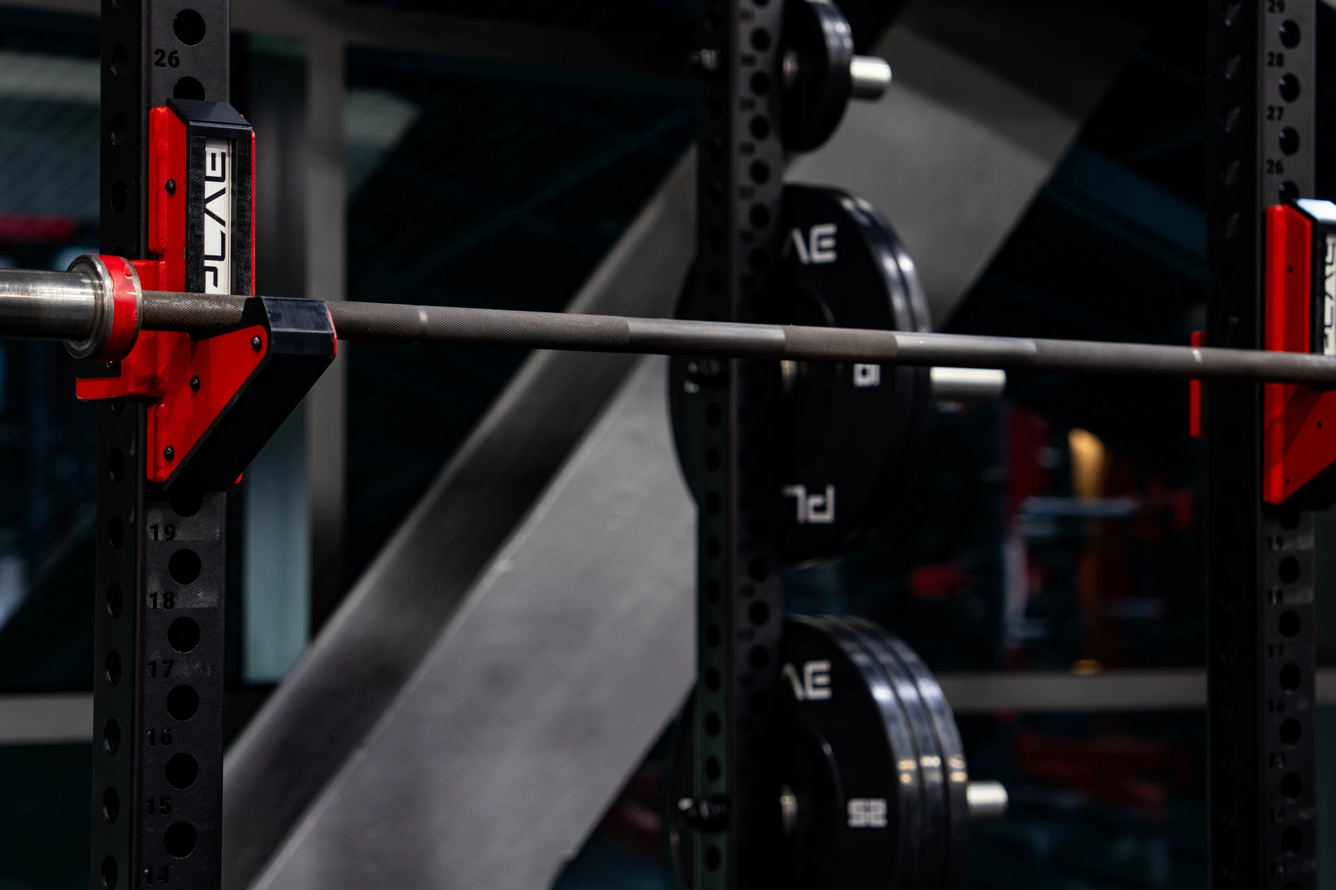 Close-up of a PLAE Olympic barbell resting on custom ICONx J-cups within a custom strength training station.
