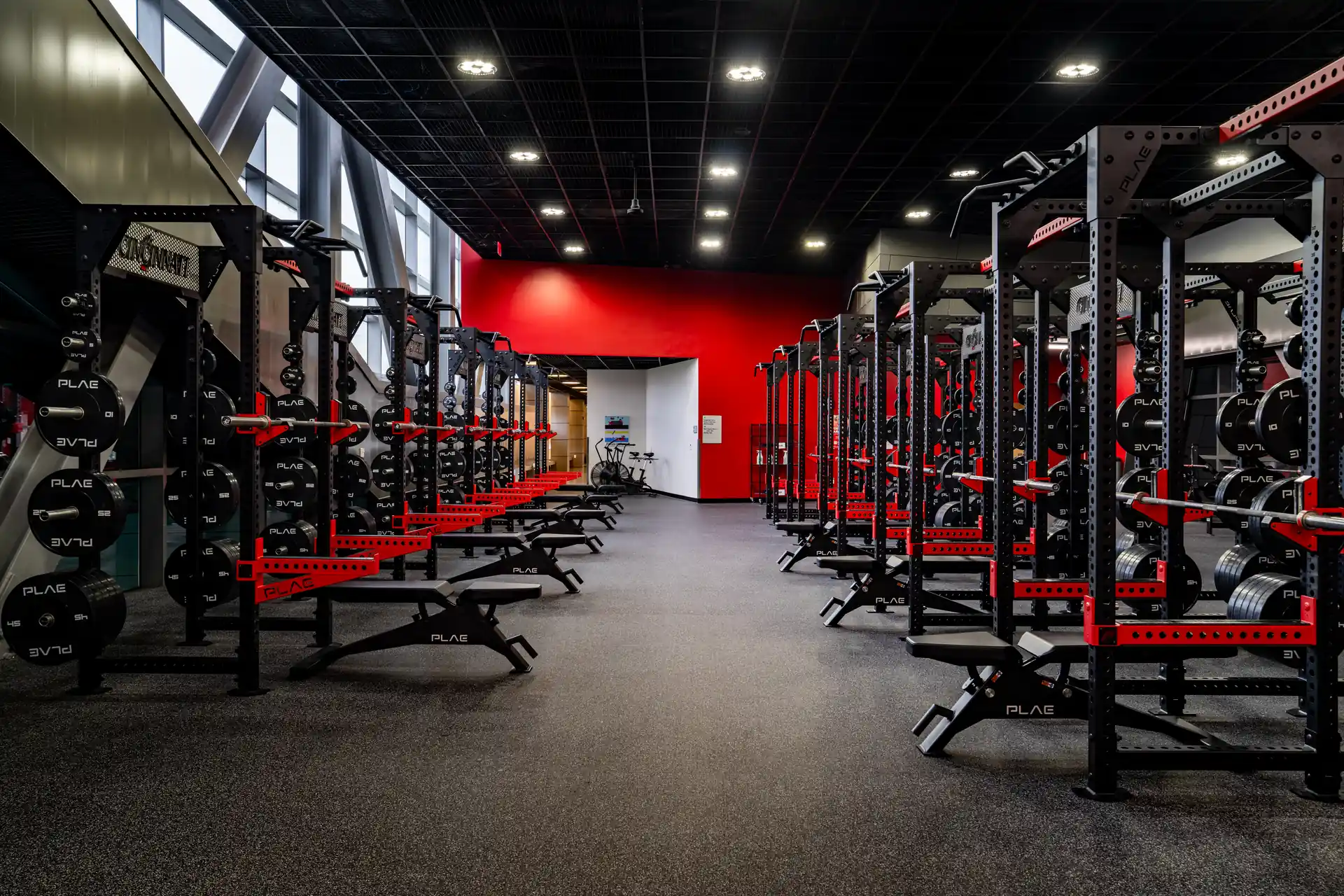 Rows of custom PLAE ICONx racks with integrated flat benches and weight storage inside a collegiate strength training facility.