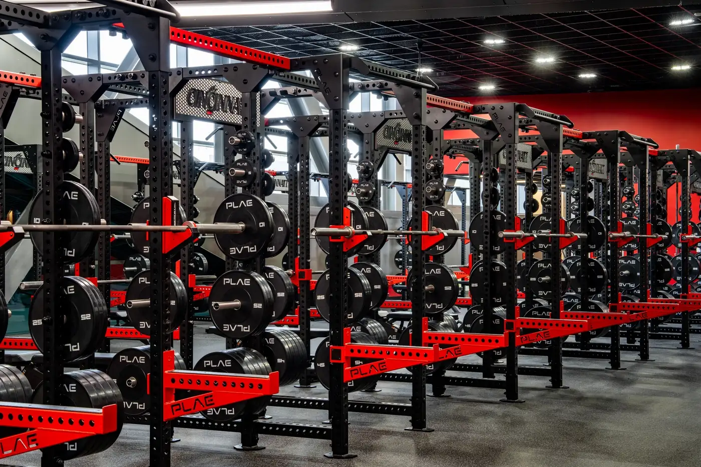 Row of custom PLAE ICONx strength racks with integrated weight storage and custom branded nameplates in a collegiate performance facility.