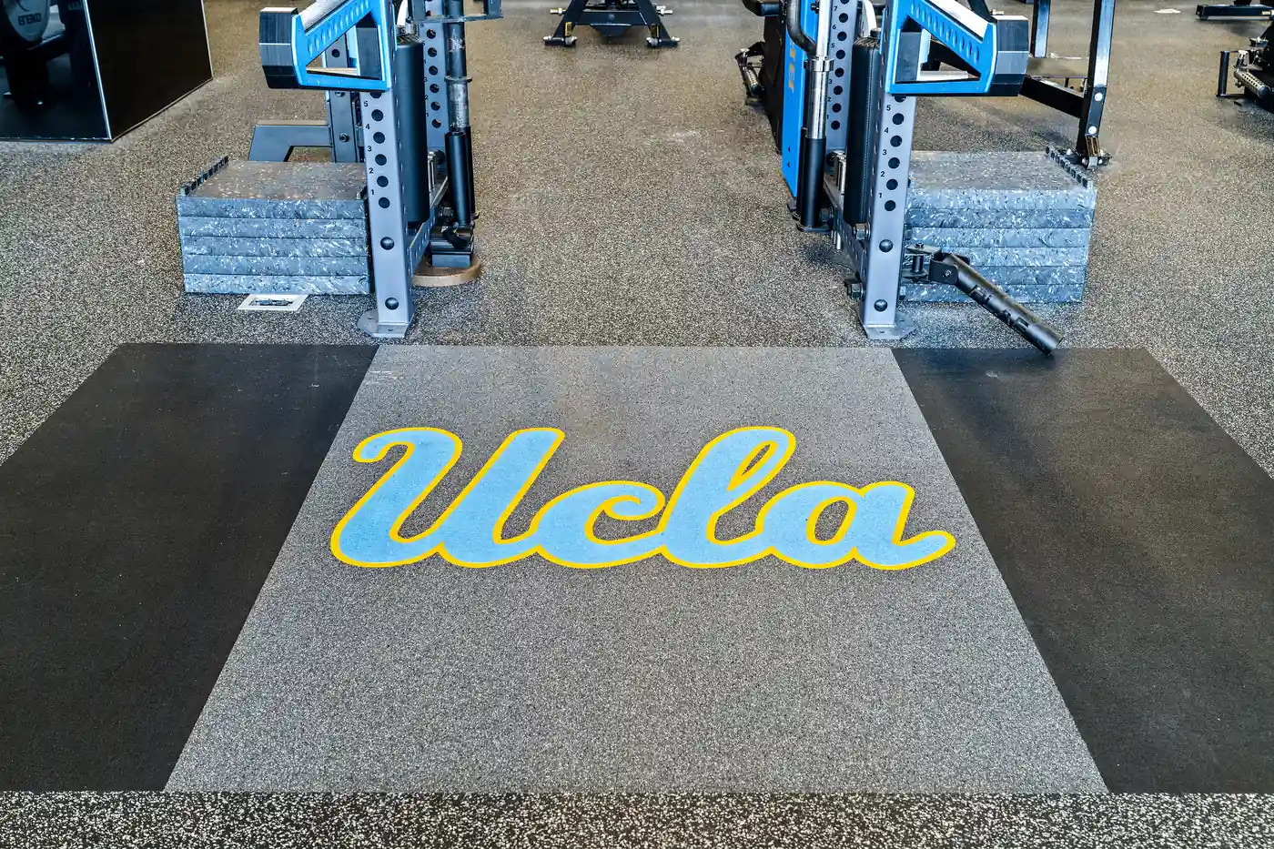 UCLA-branded weightlifting platform between two blue power racks inside the university's strength and conditioning facility.