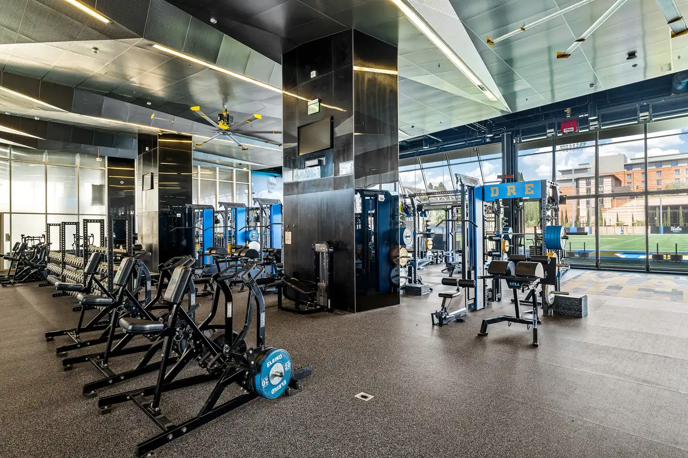 Open gym floor with UCLA cable machines, strength equipment and floor-to-ceiling windows.