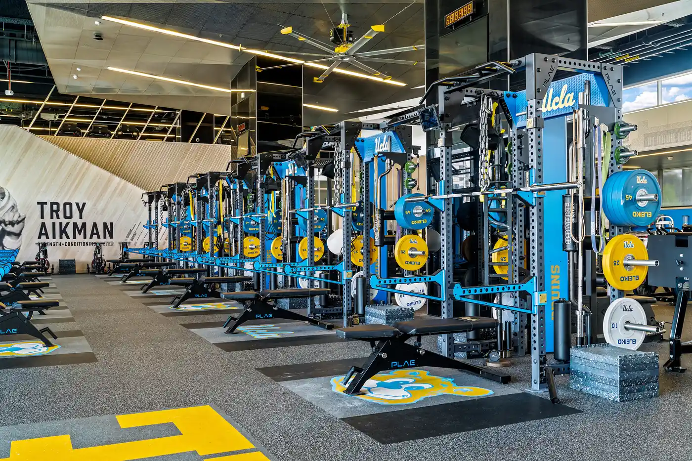 Wide interior of the UCLA strength training facility featuring multiple PLAE power racks and lifting platforms.