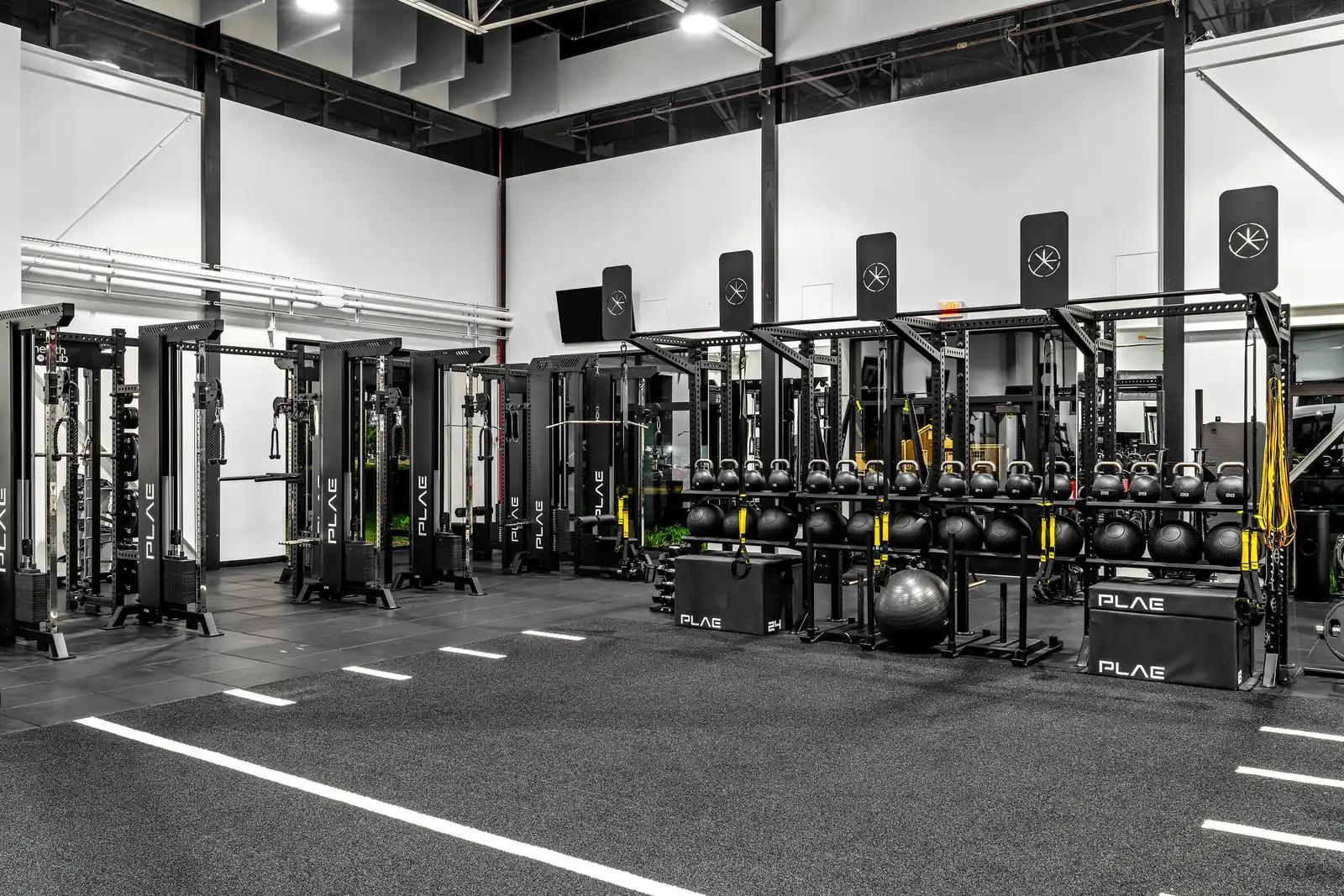 PLAE power racks and functional rig with competition kettlebells, slam balls, TRX straps and branded PLAE plyo boxes in the functional training area.