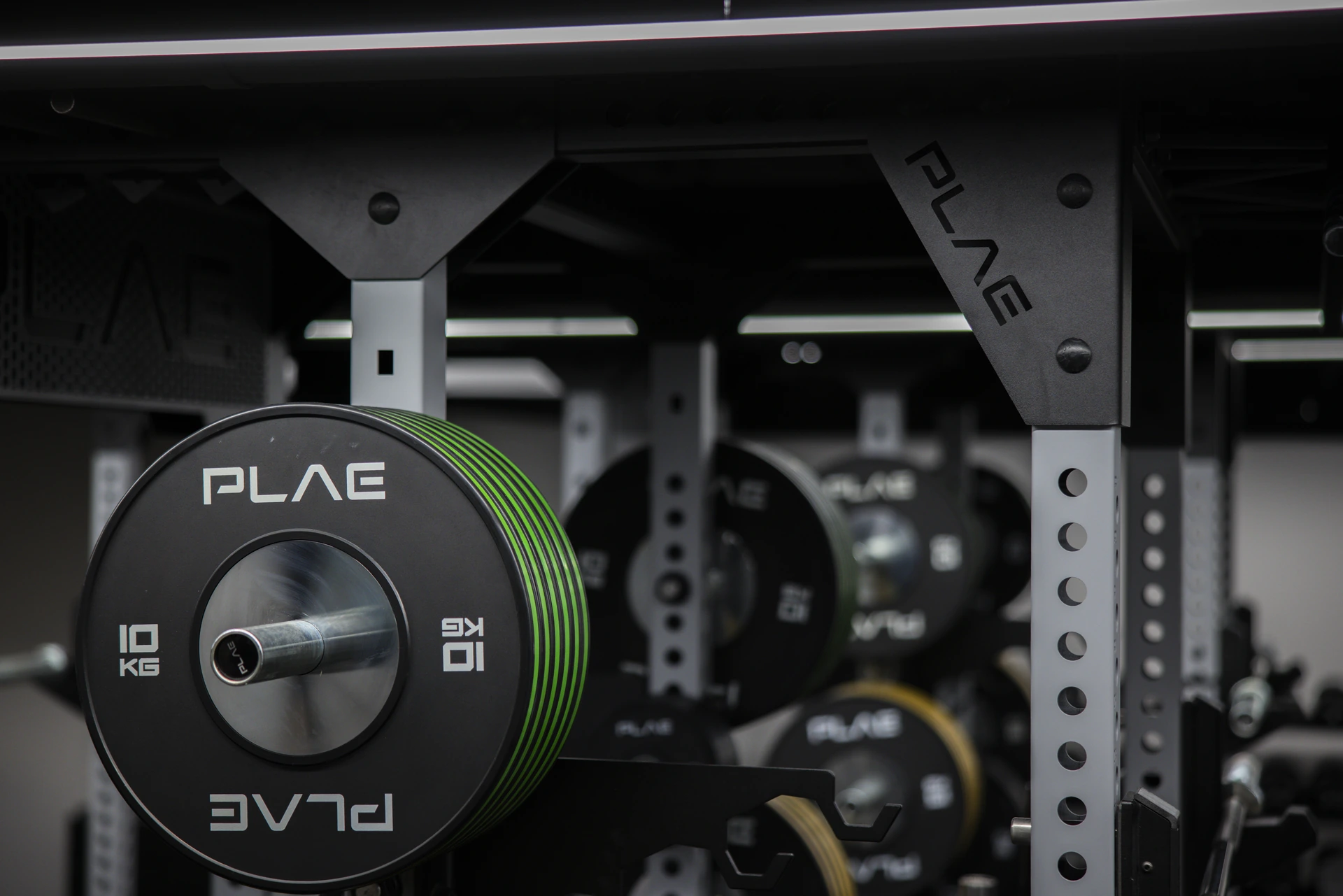 Loaded barbell with a green PLAE bumper plate racked on an ICONx rack at Athletes Authority