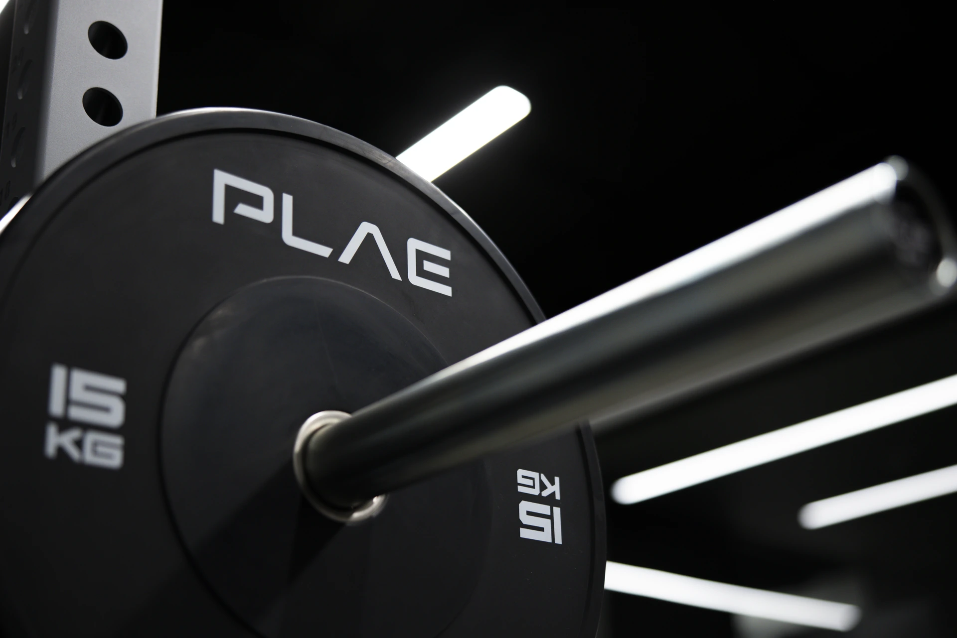Low-angle view of a barbell loaded with PLAE bumper plates under linear lights