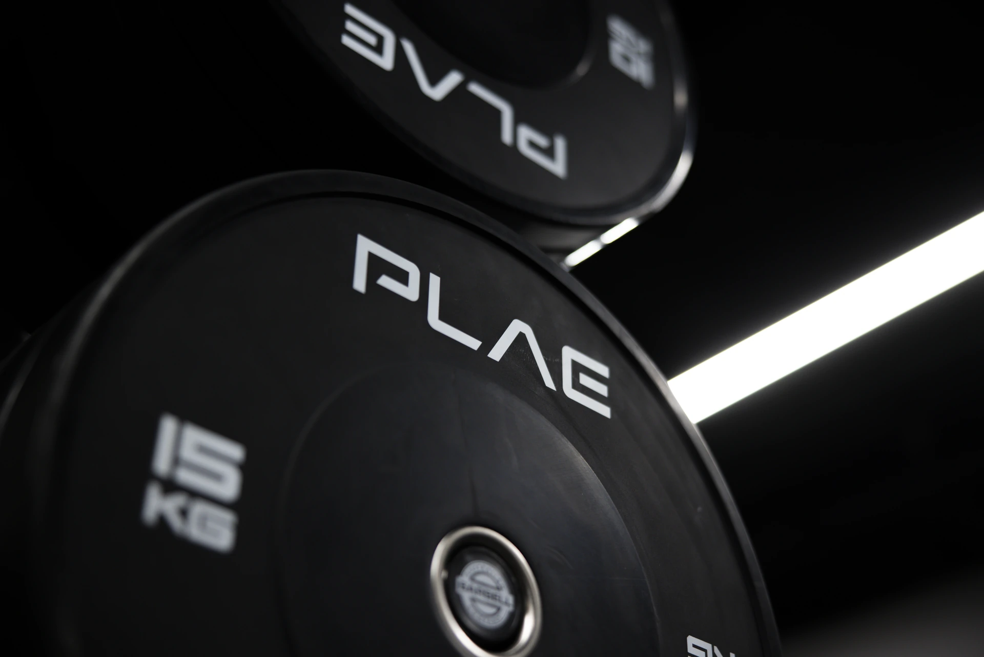 Close-up of a black 15kg PLAE bumper plate under linear lighting