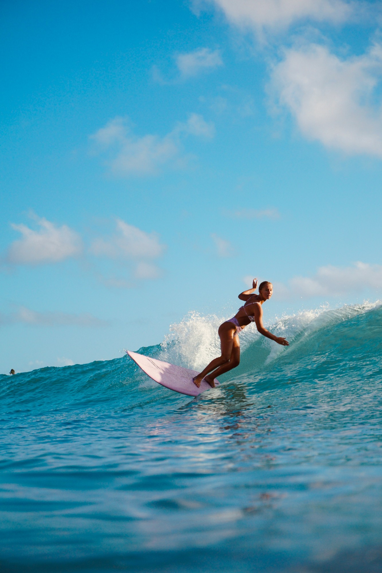 A surfer riding a clean turquoise wave under a blue sky