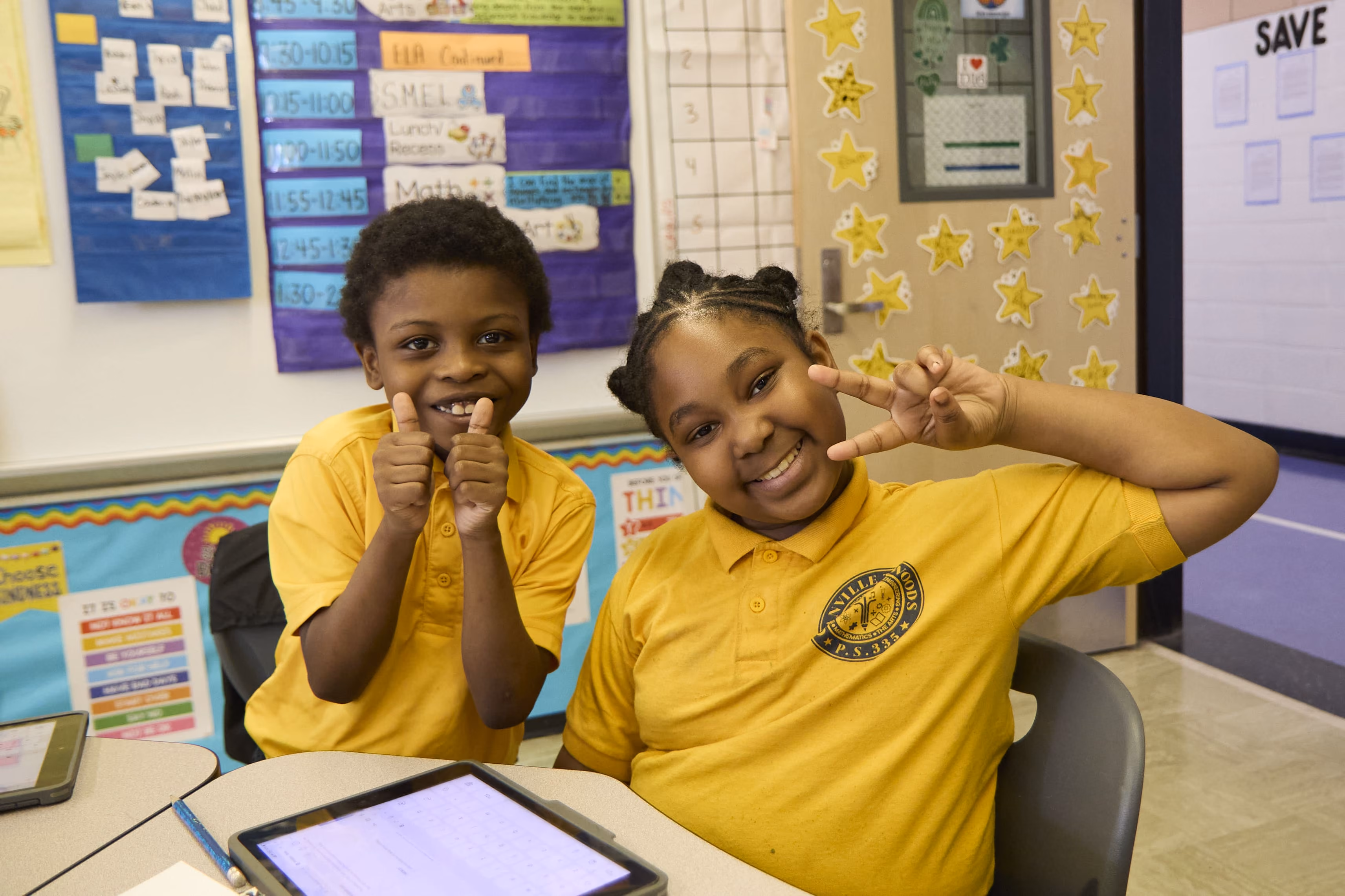 Two smiling students in yellow uniforms posing at classroom desk