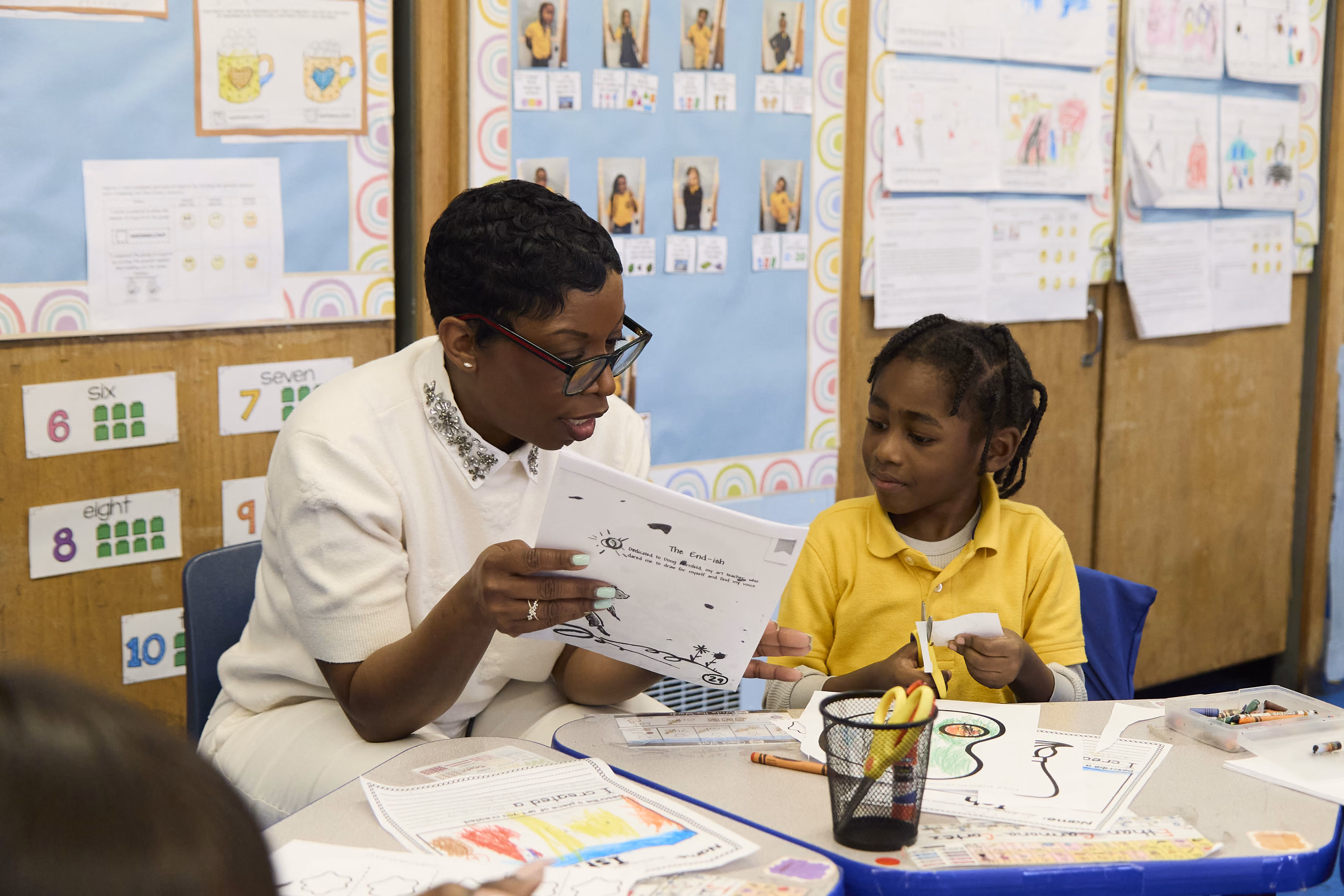Teacher reviewing student drawing with young girl in classroom