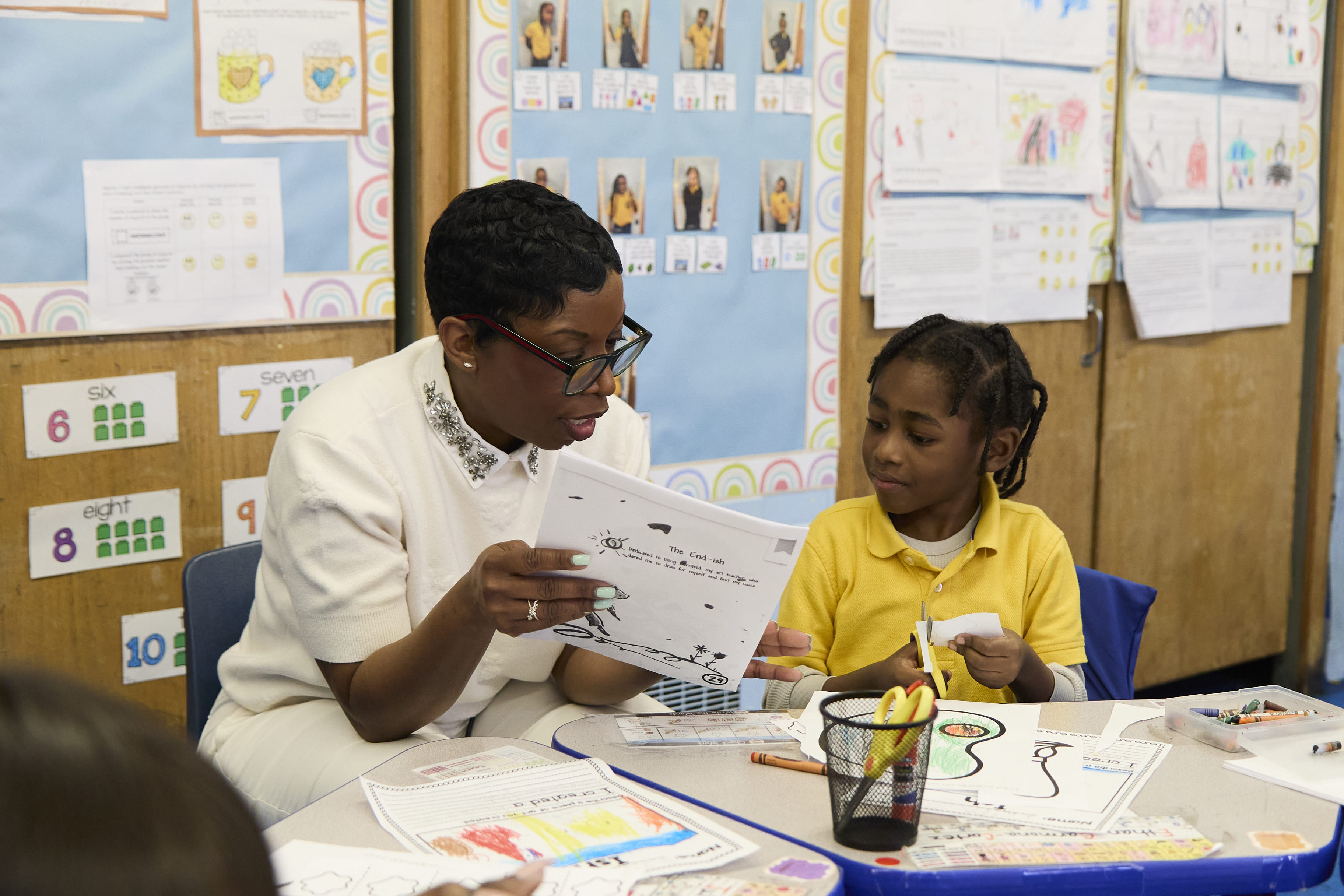 Teacher reviewing student drawing with young girl in classroom