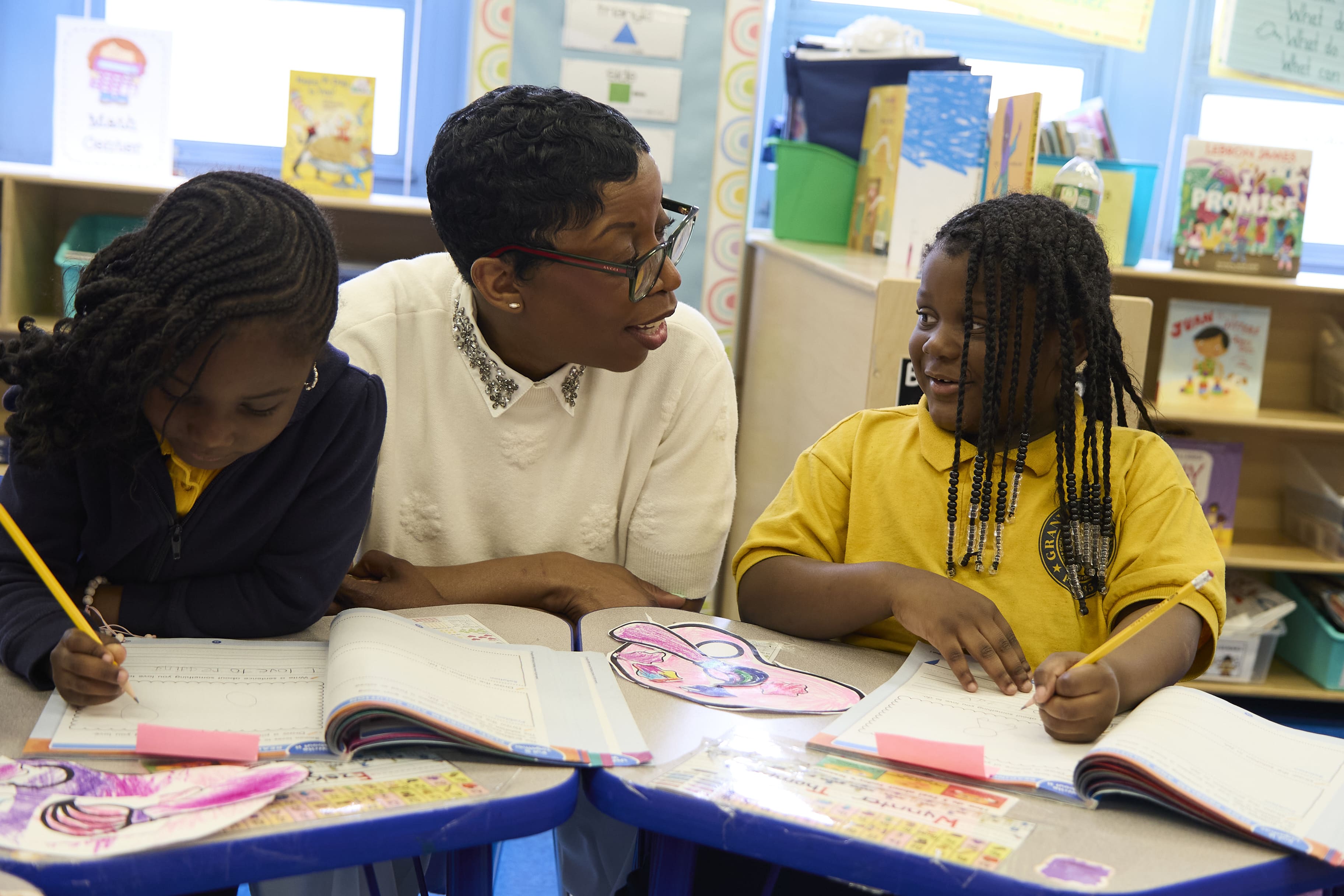 Teacher smiling with two elementary students during a writing activity