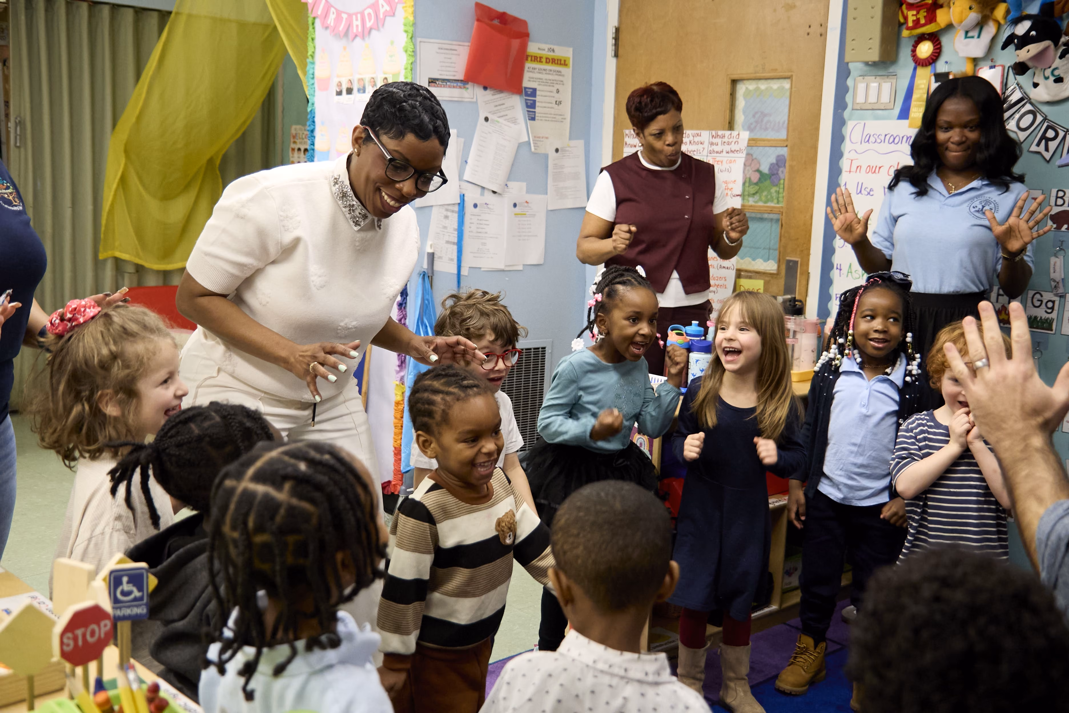 Adults and young children laughing together during an energetic classroom activity