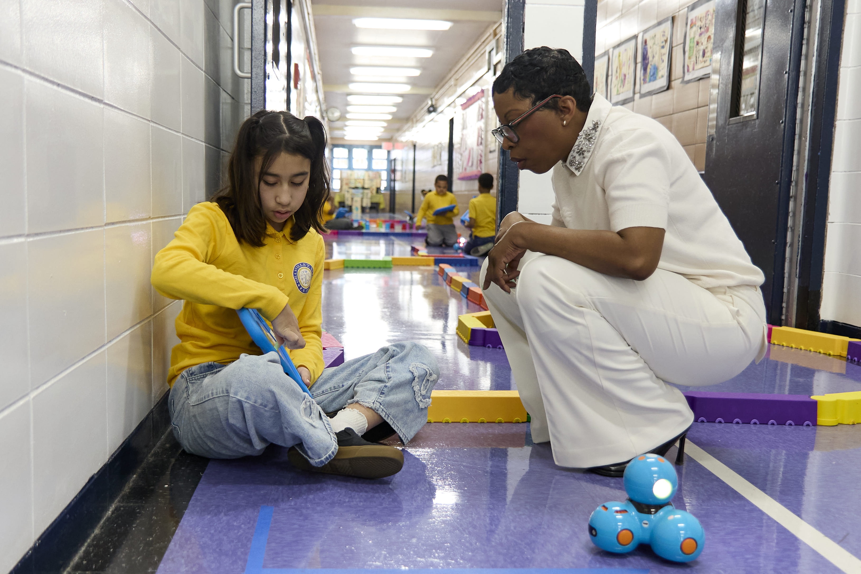 Teacher guides student using tablet to program robot in hallway