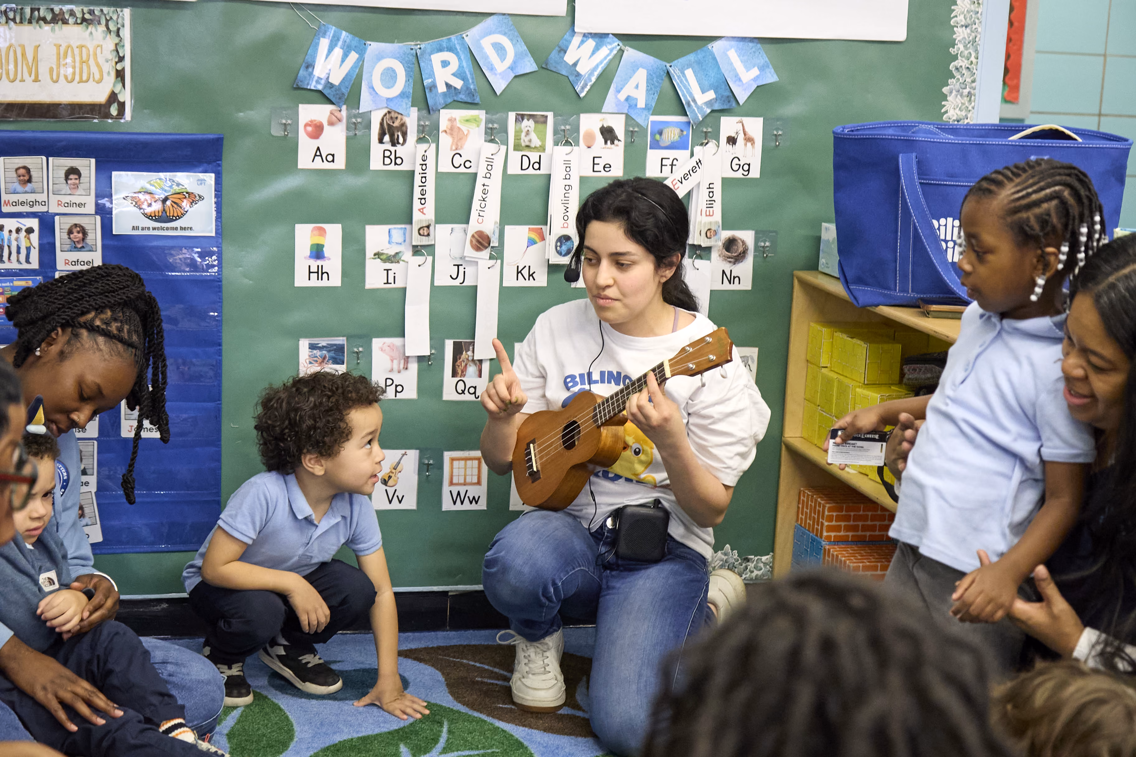 Teacher playing ukulele for young students near classroom word wall