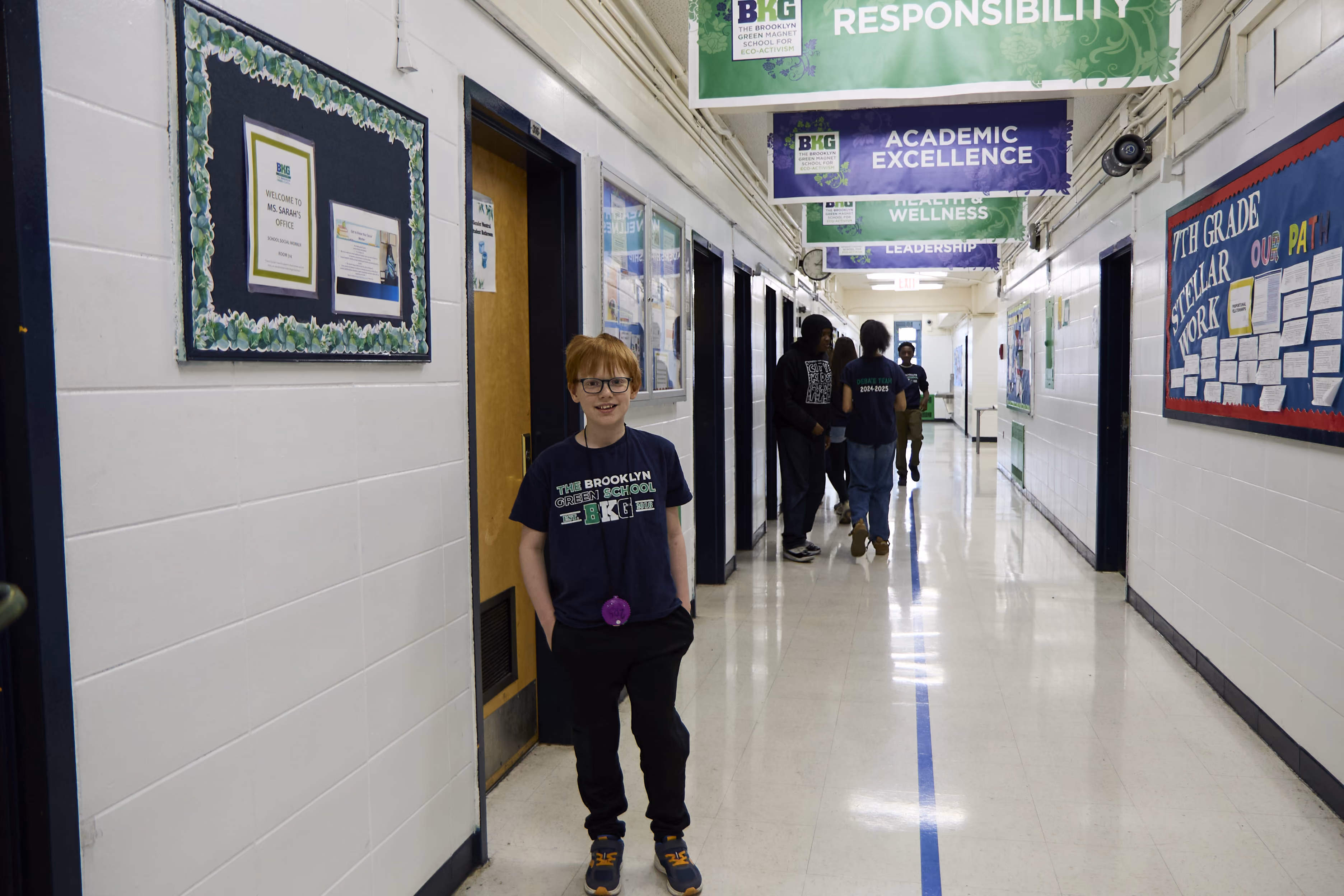 Student smiling in Brooklyn Green School hallway with academic banners