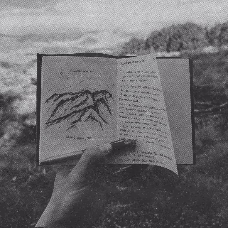 a hand holding a journal with a sketch of a mountain