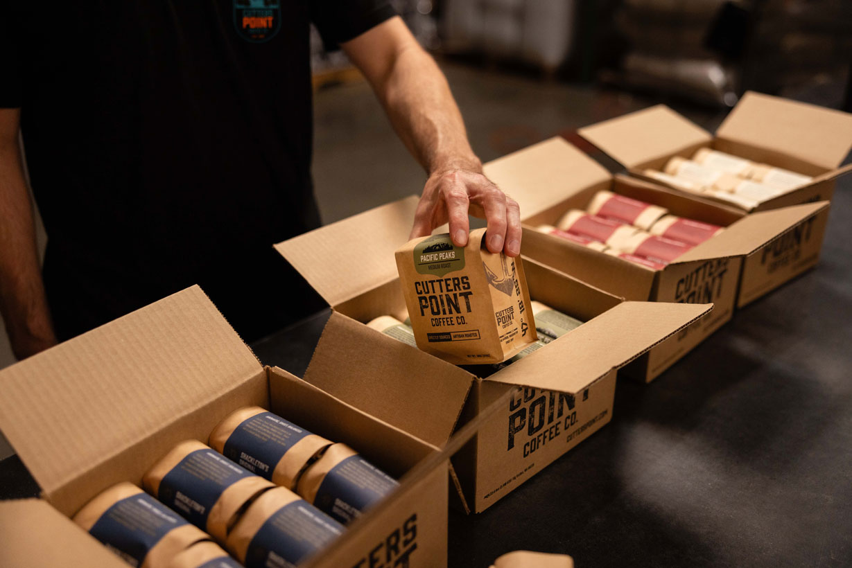 Hand packing Cutters Point Wholesale Coffee bags into shipping boxes inside the PNW Cutters Point Coffee roastery.