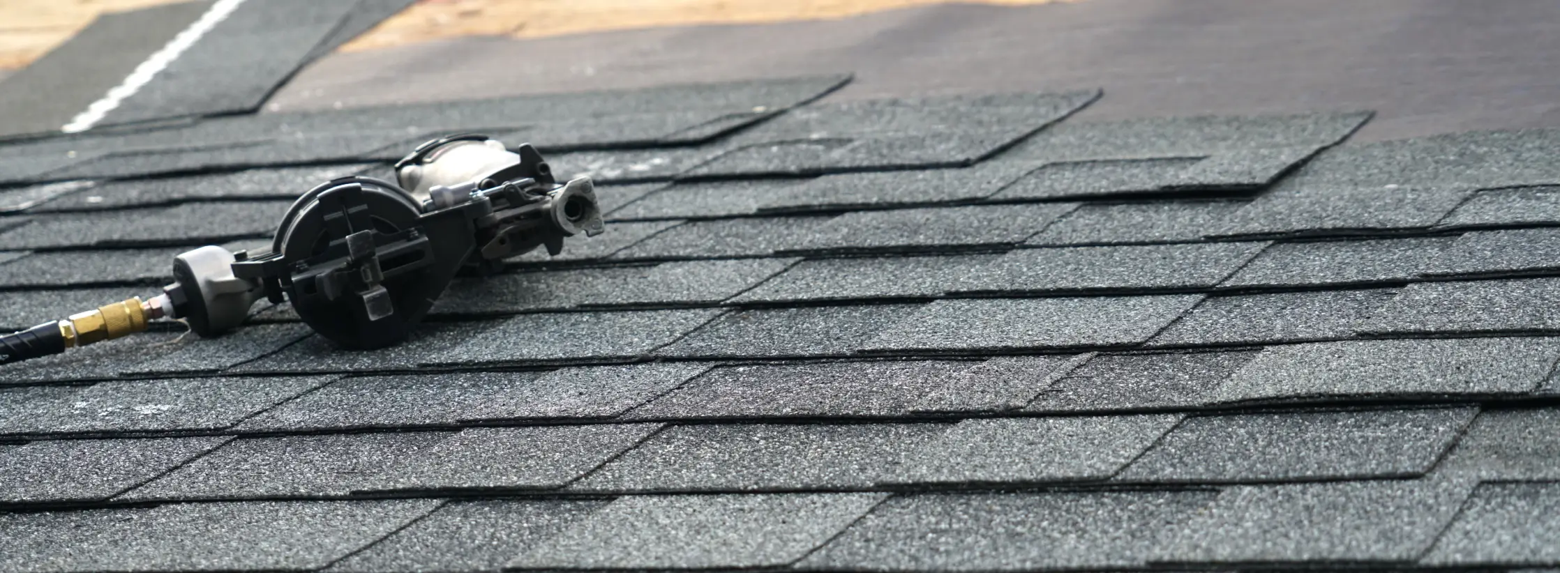 Pneumatic roofing nailer resting on newly installed asphalt shingles during roof work.