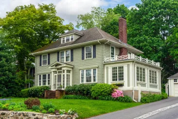 sage green colonial two-story home with white trim and lush landscaping