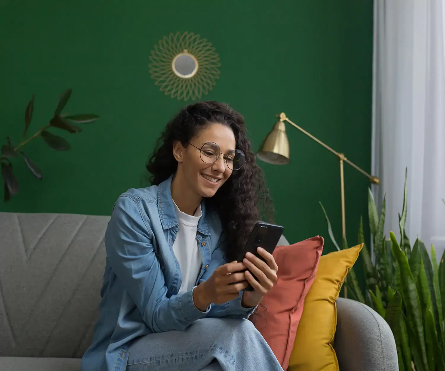A smiling woman sitting on a sofa and using her smartphone for a virtual consultation