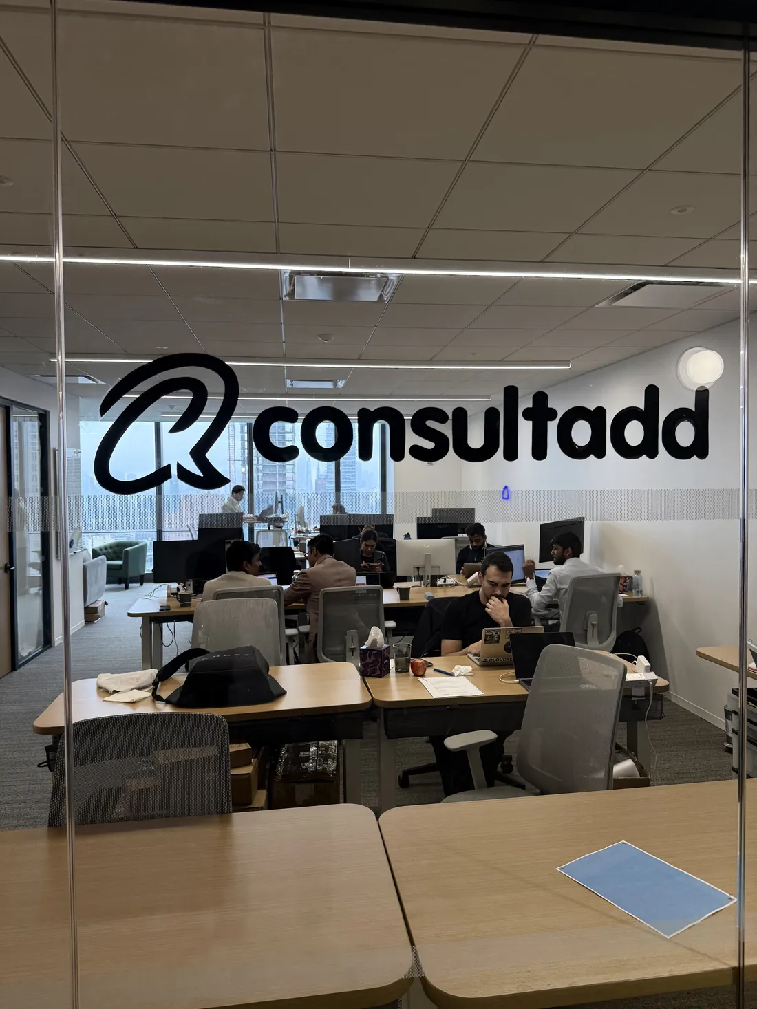 Consultadd logo on the glass entrance of the New York office, with the team working at their desks inside