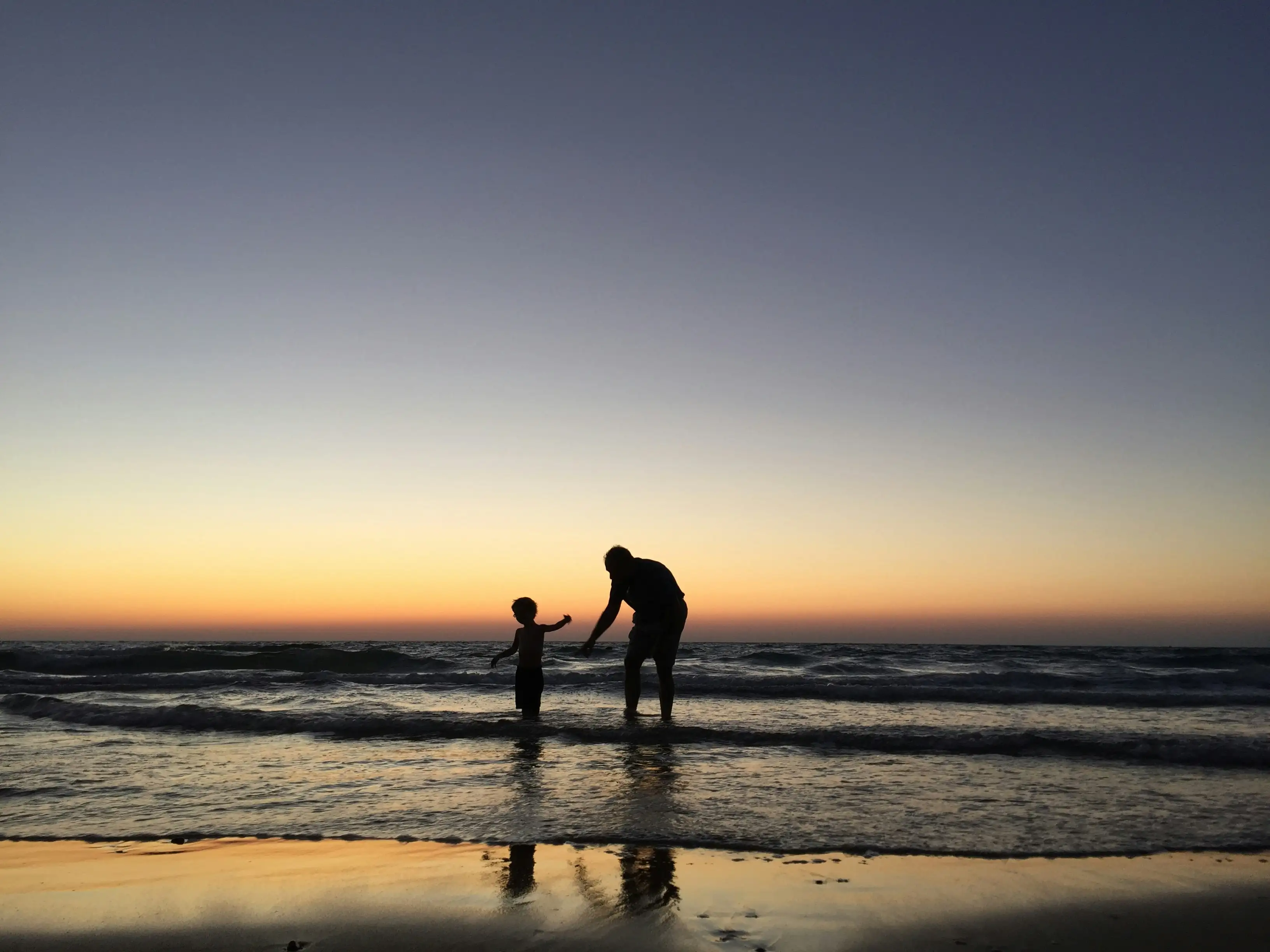 A child and parent playing during sunset on the beach shore