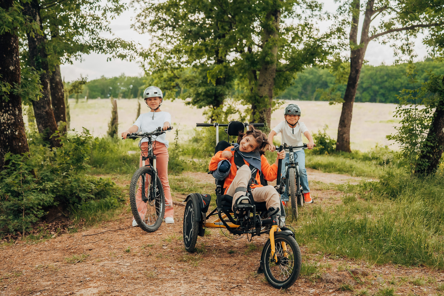 Ein Mädchen fährt das Therapierad Trix von Hase Bikes mit ihren Freunden durch den Wald.