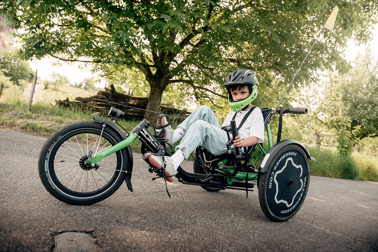 Das Therapierad Trets, ein grünes Dreirad wird von einem Junge mit Helm sportlich gefahren
