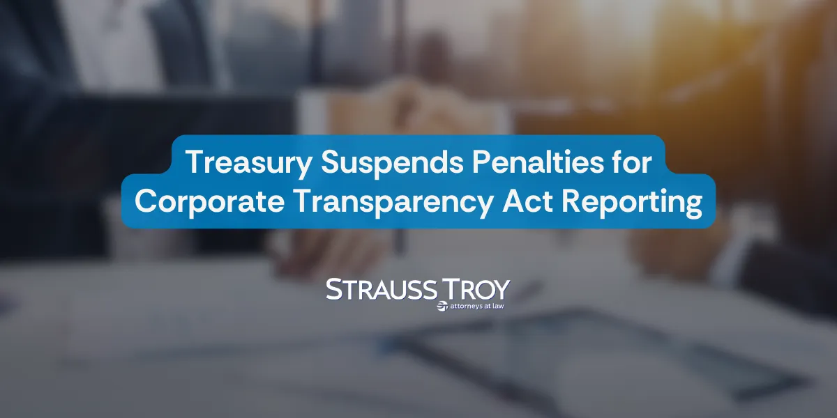 "Treasury Suspends Penalties for Corporate Transparency Act Reporting" in bold white text on a blue background, with a blurred office setting in the background. Strauss Troy logo displayed below.