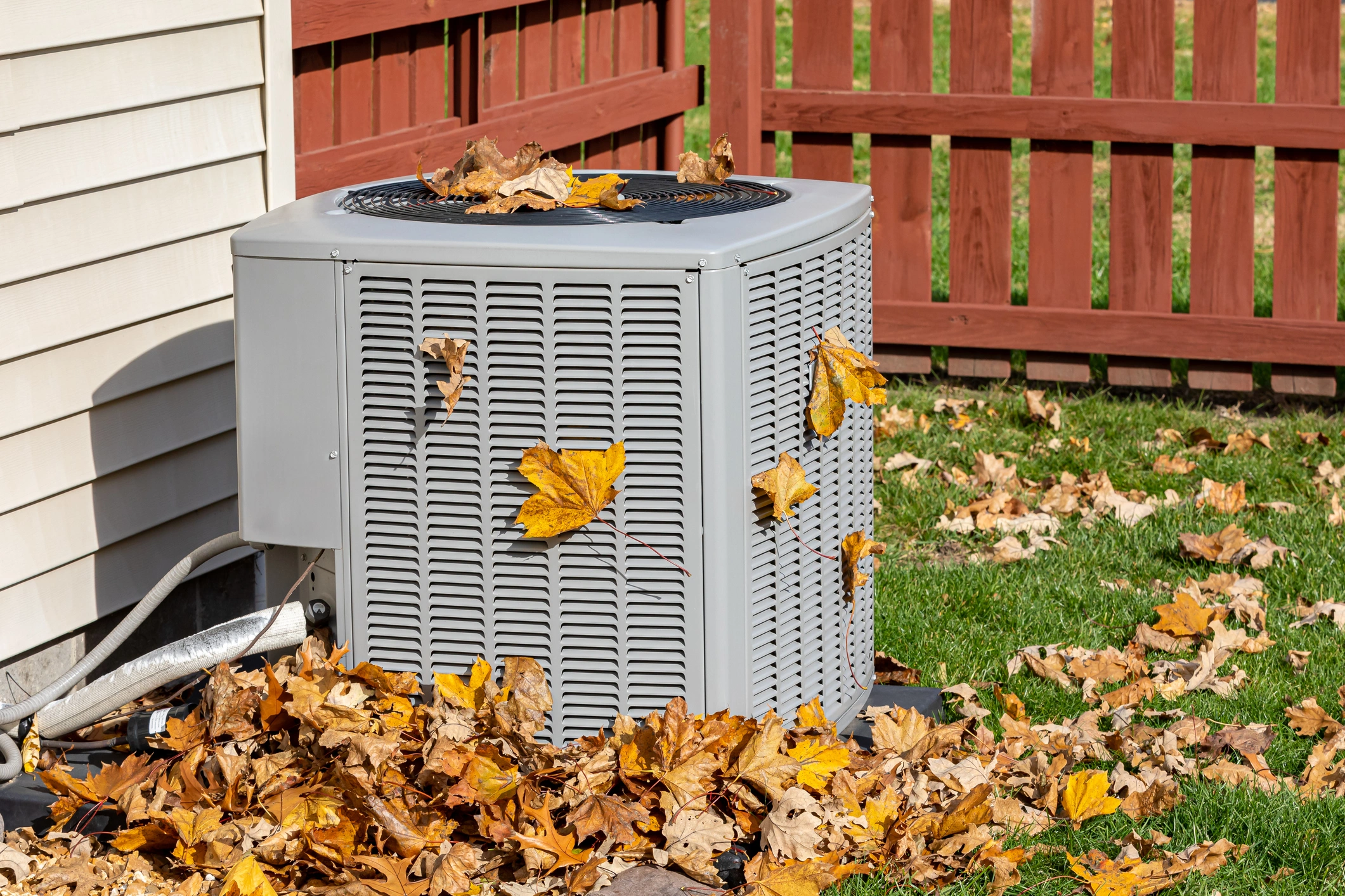 Outdoor air conditioning unit covered with scattered autumn leaves.