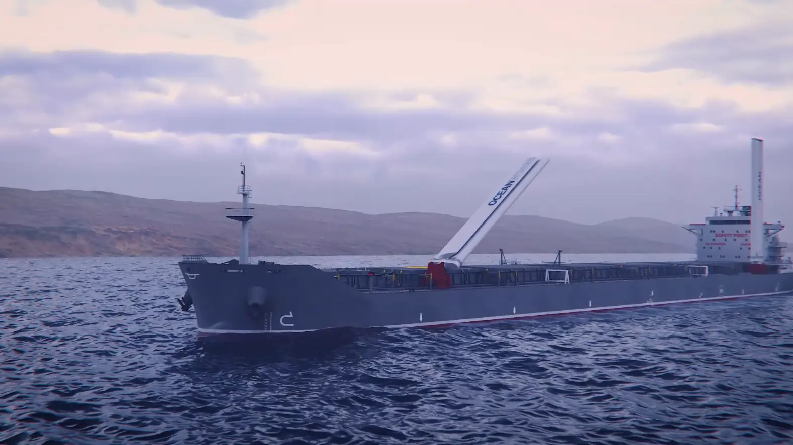 Large cargo ship equipped with vertical wind propulsion technology sails on calm waters near a hilly coastline under an overcast sky.