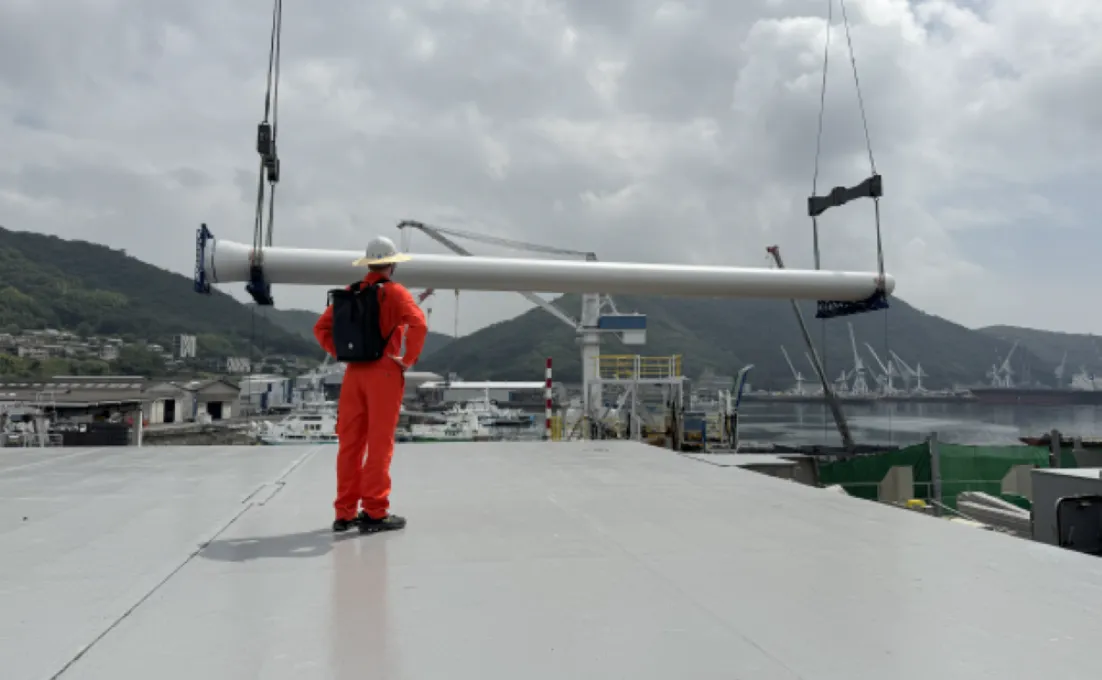 A boom and the bottom part of the sail of a rigid wing sail from OceanWings, with a blue sky on the background.